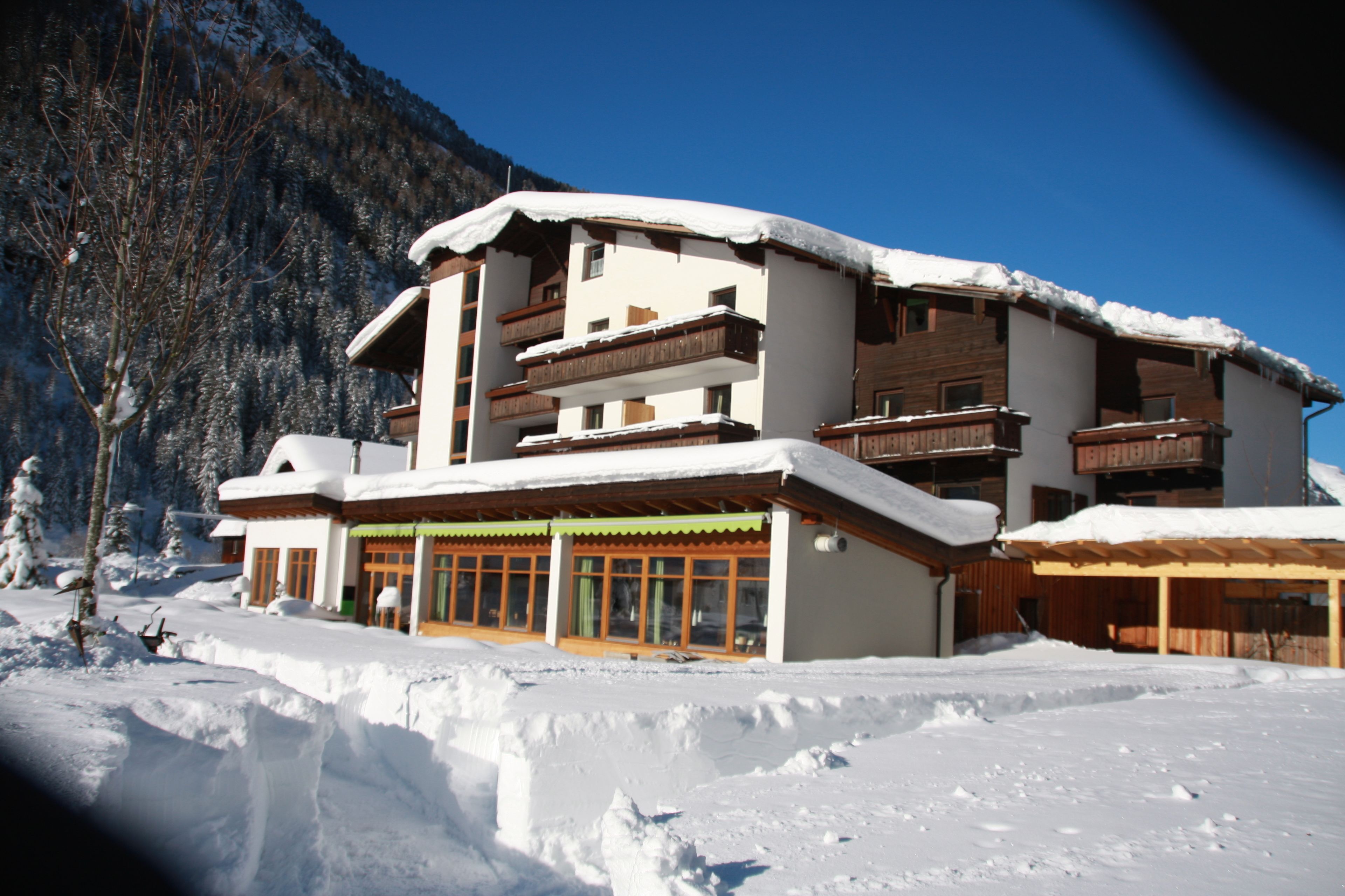 A multi-story building with balconies, surrounded by snow-covered ground and mountains.