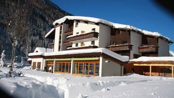 A multi-story building with balconies, surrounded by snow-covered ground and mountains.
