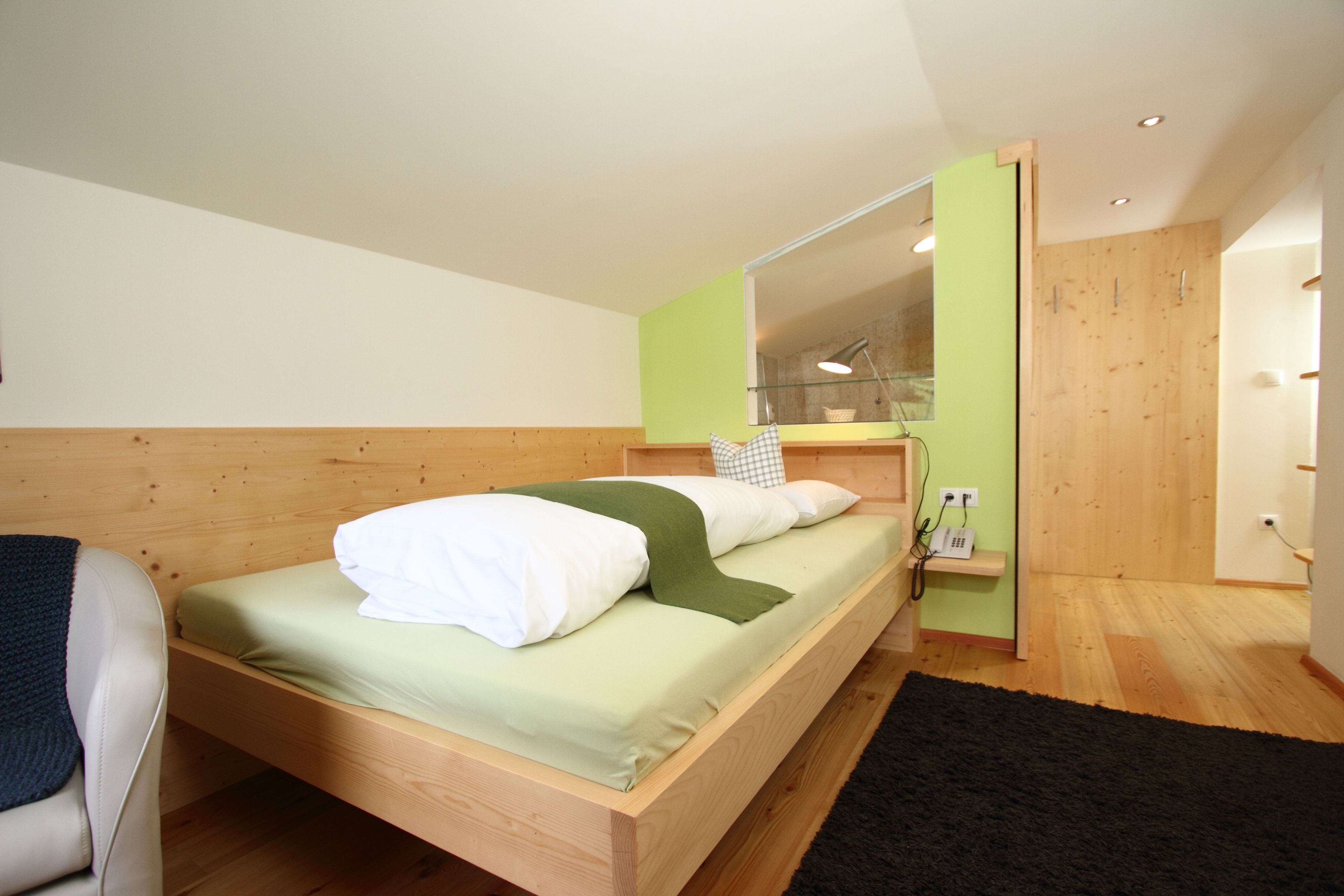 A modern bedroom with a wooden bed, a green wall, and a mirror.