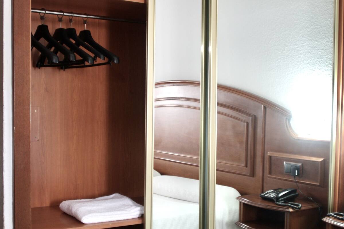 A hotel room with a wooden wardrobe, a bed with white bedding, and a bedside telephone.