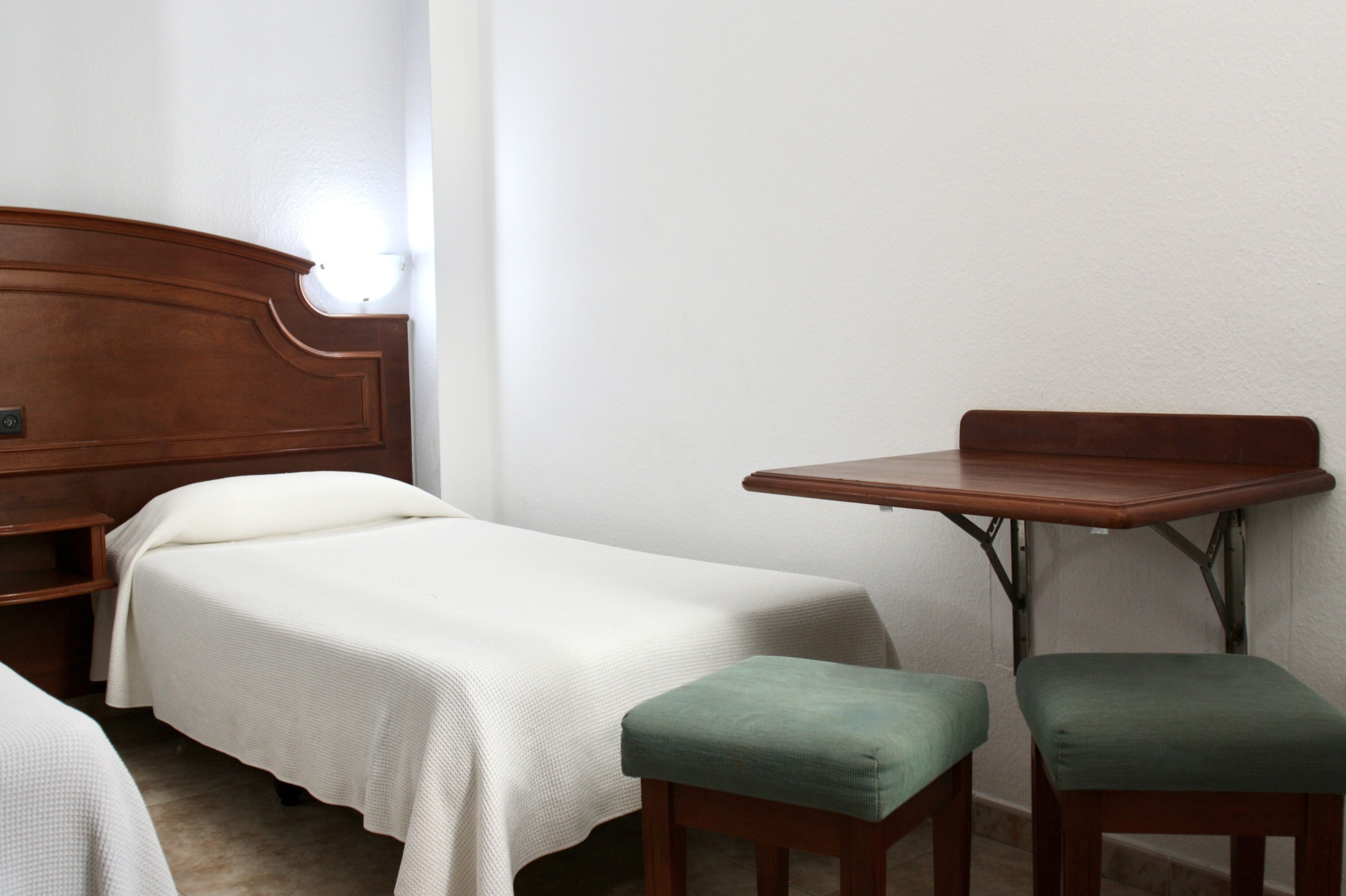 A small, simple room with a single bed, a small table, and two chairs.
