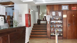 A reception area with a wooden reception desk, a staircase, and a bookshelf with various items. - Tropical (Puerto de la Cruz)