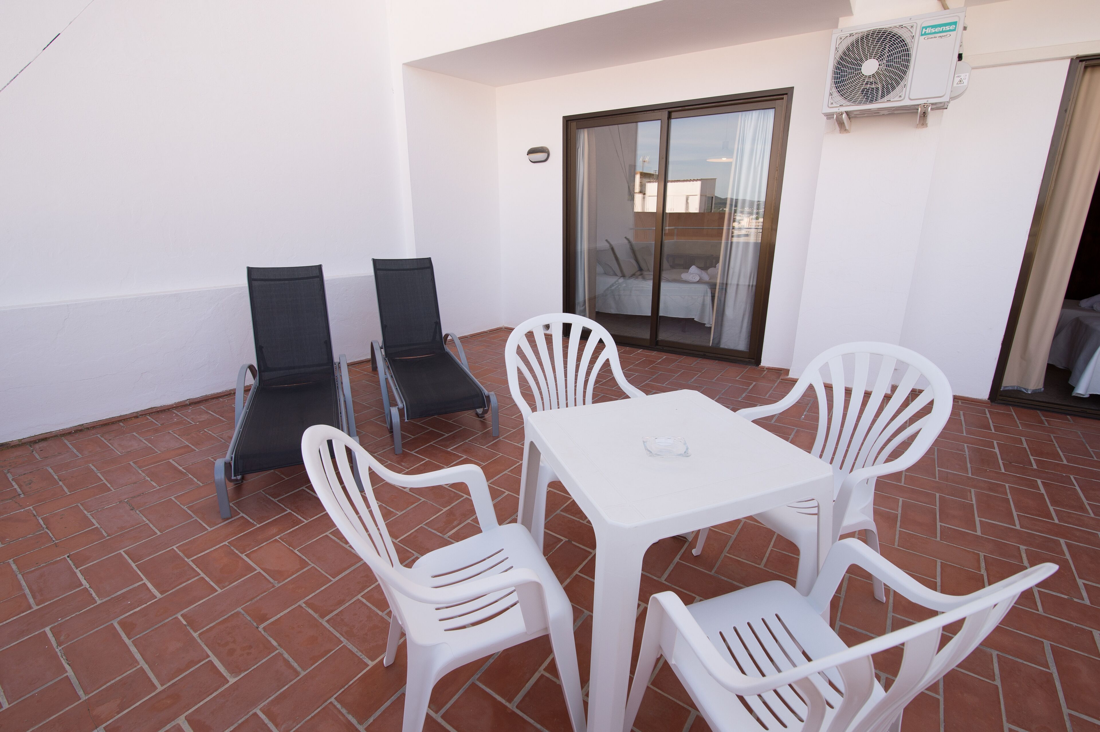 A patio with a white table and four white chairs, two black chairs, and a sliding glass door.