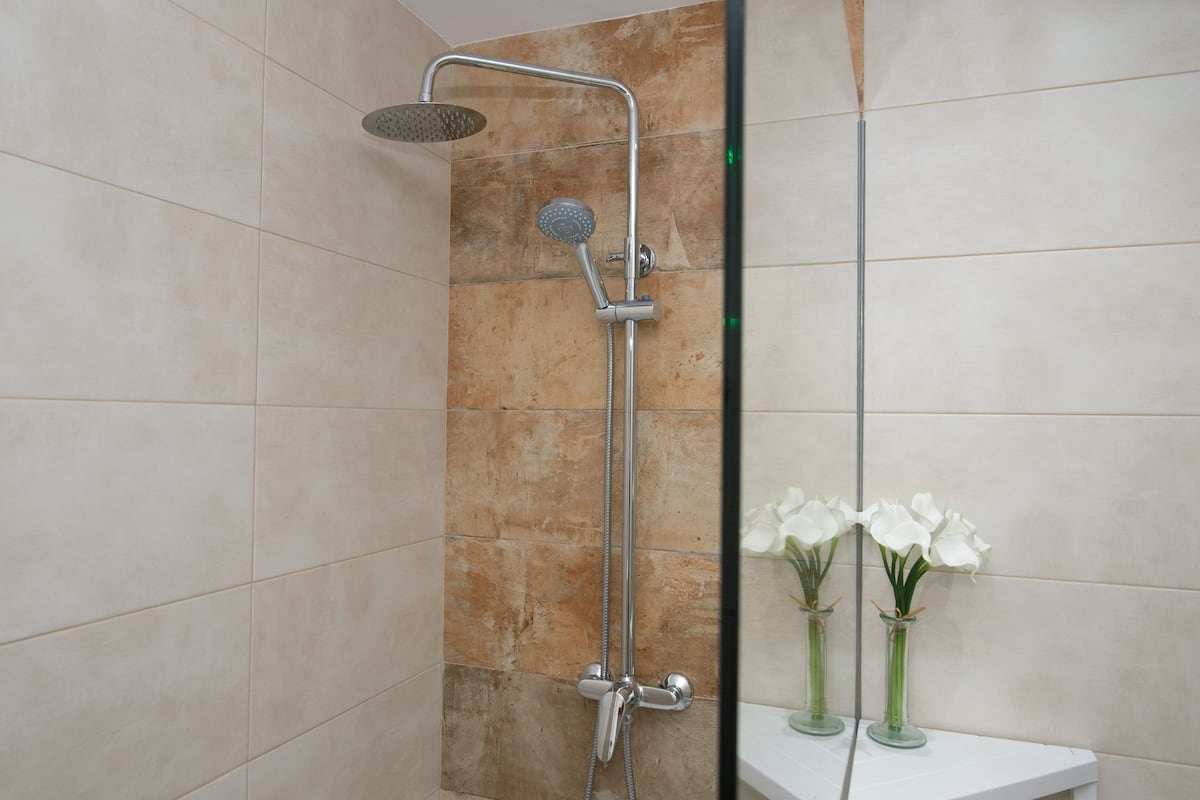 Ducha con cabezal de ducha manual y grifo empotrado en la pared. Hay dos jarrones con flores blancas sobre una superficie blanca.