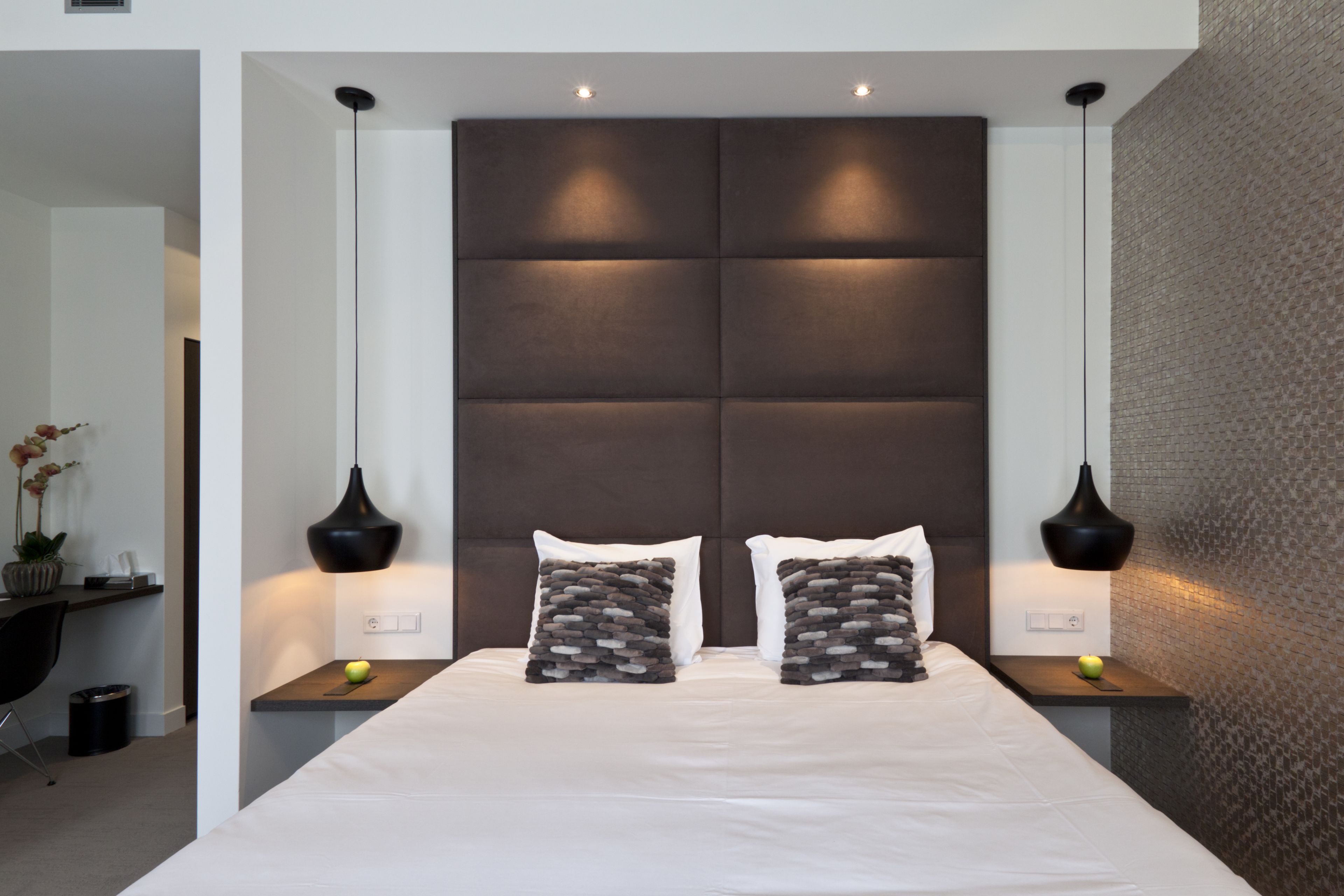 A modern bedroom with a large bed, two bedside tables, and a headboard with integrated lighting.