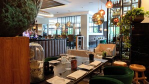 Un comedor con una mesa larga dispuesta para una comida, rodeado de sillas tapizadas de verde y una zona de bar con botellas y vasos.