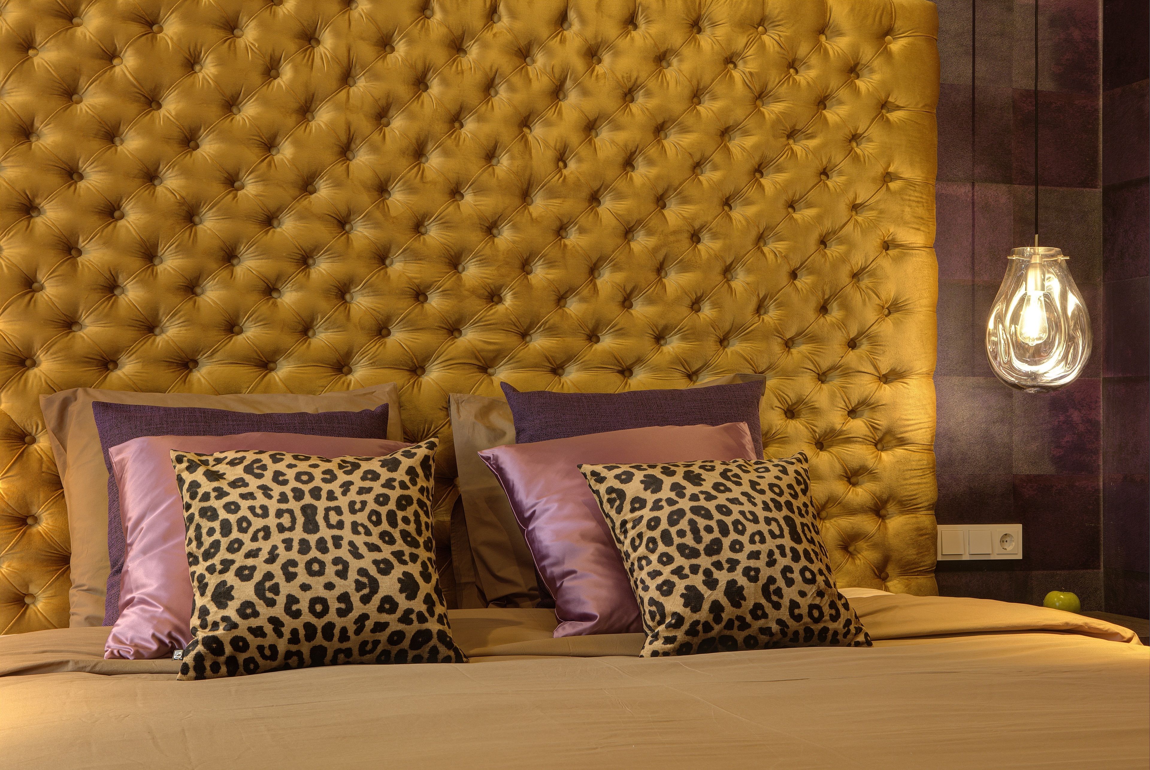 Cabecera tapizada con diseño capitonado, dos almohadones de estampado de leopardo y una lámpara colgante.