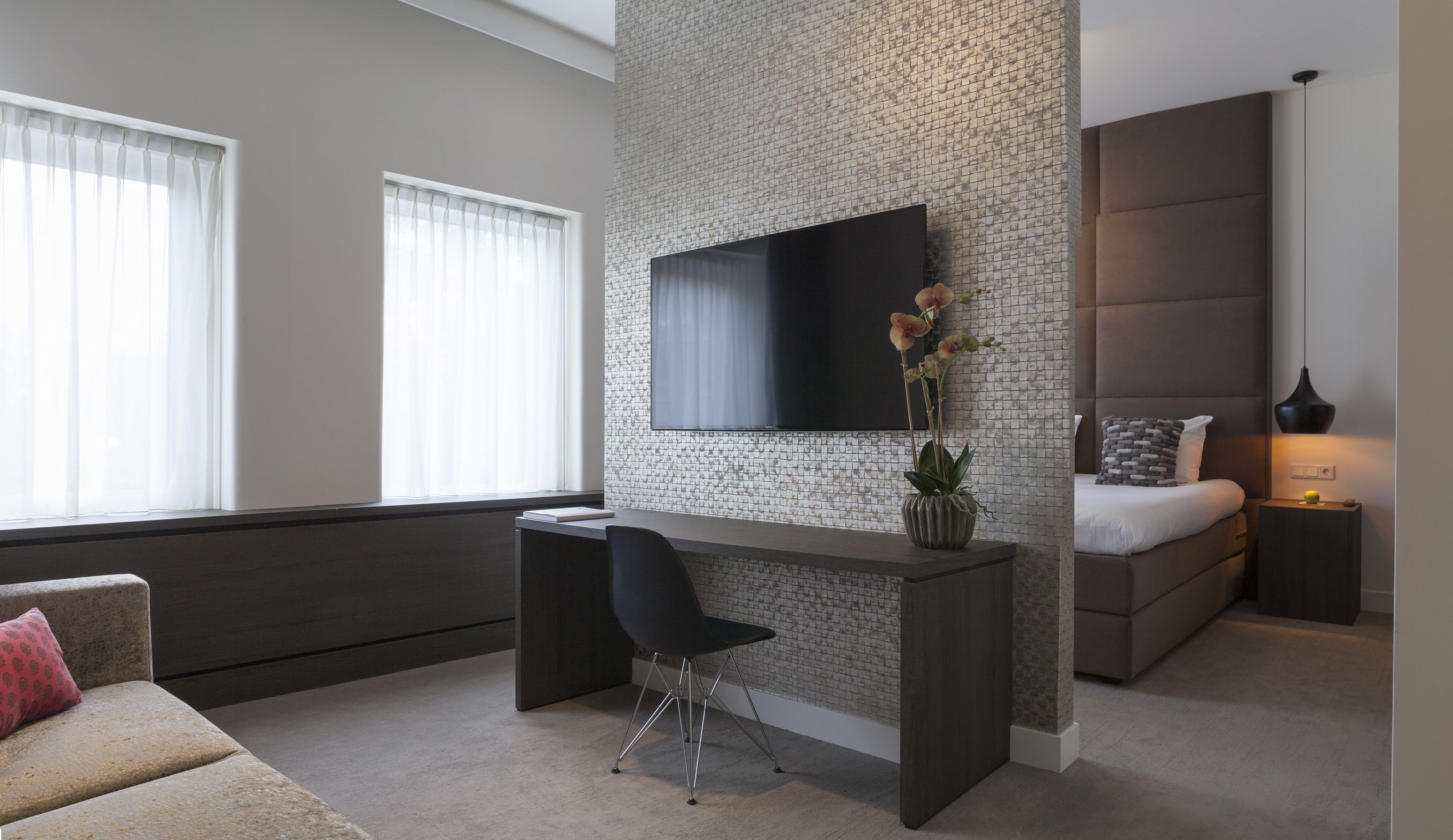 Une chambre moderne dotée d’un bureau intégré, d’un téléviseur à écran plat, d’un lit avec une tête de lit et d’une table de chevet avec une lampe.