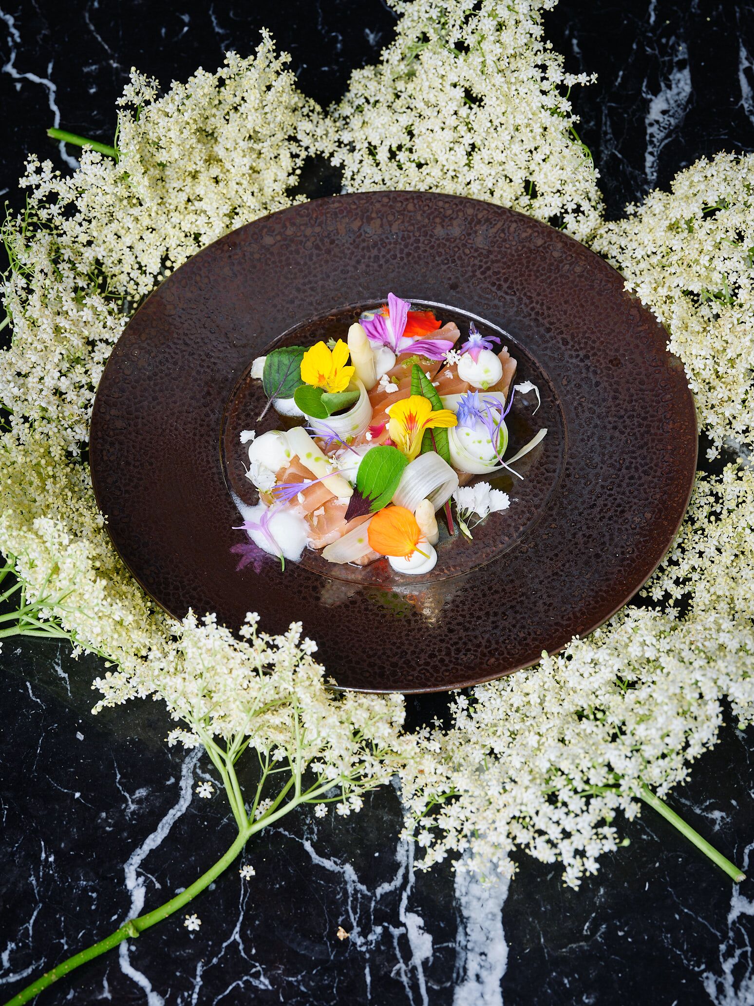 Un plato de cerámica oscura con un arreglo floral sobre una superficie de mármol negro.