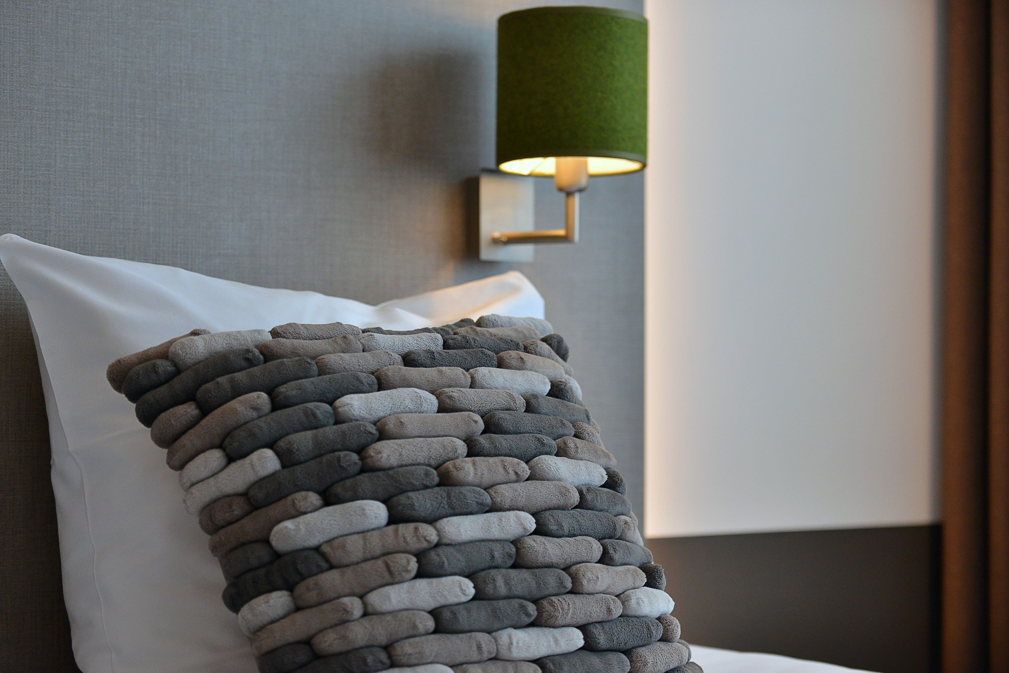 A bed with a white pillow and a textured gray blanket.