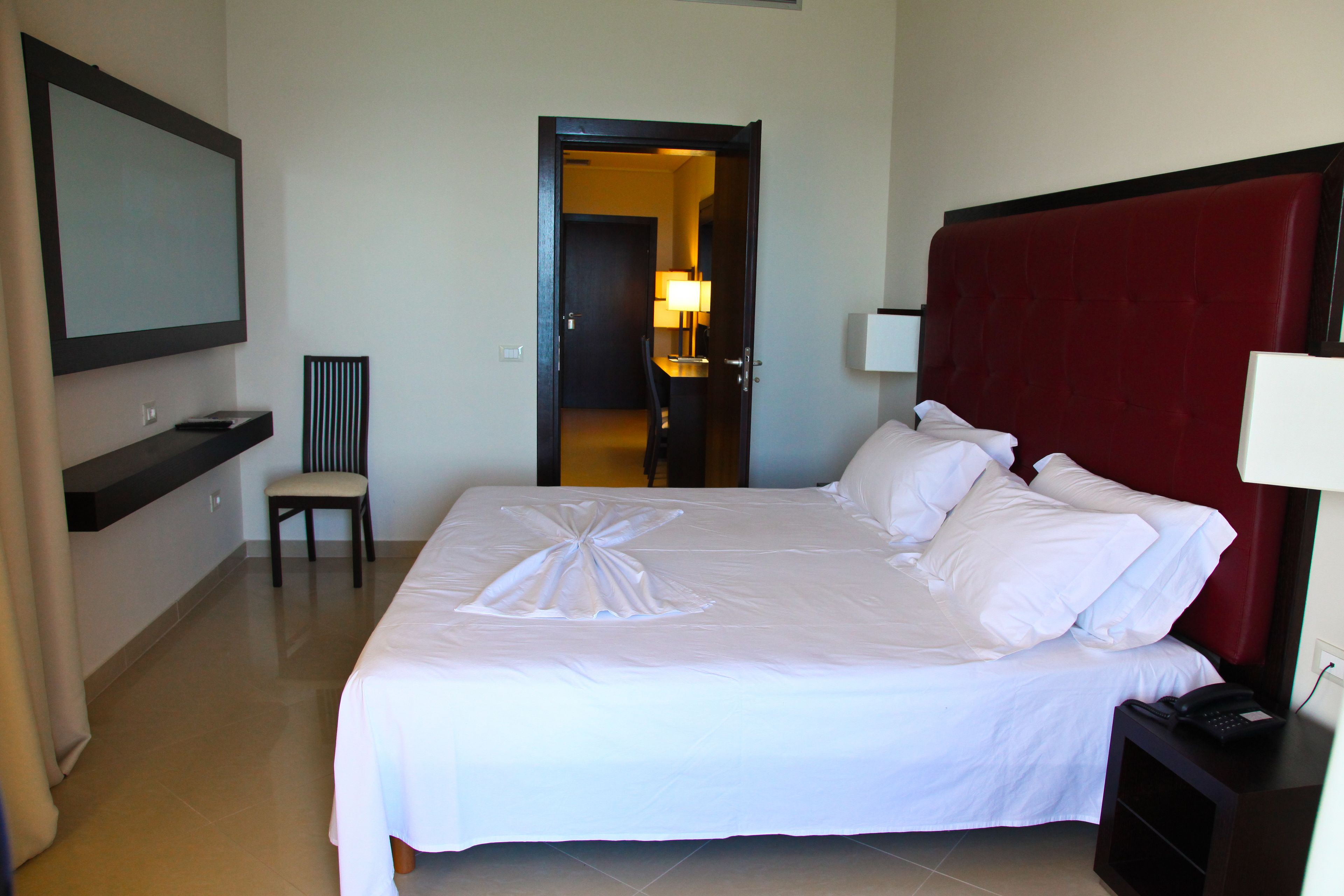 A hotel room with a neatly made bed, a chair, a desk with a lamp, and a large mirror on the wall.