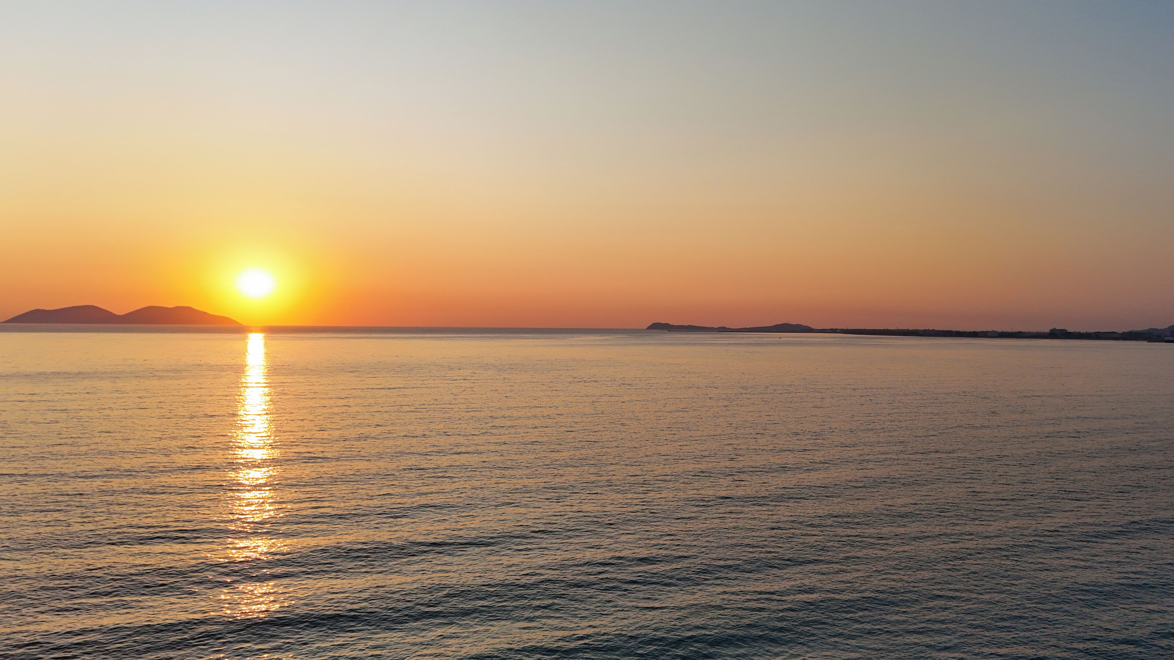 Un atardecer sobre un mar tranquilo con formas de tierra a lo lejos.
