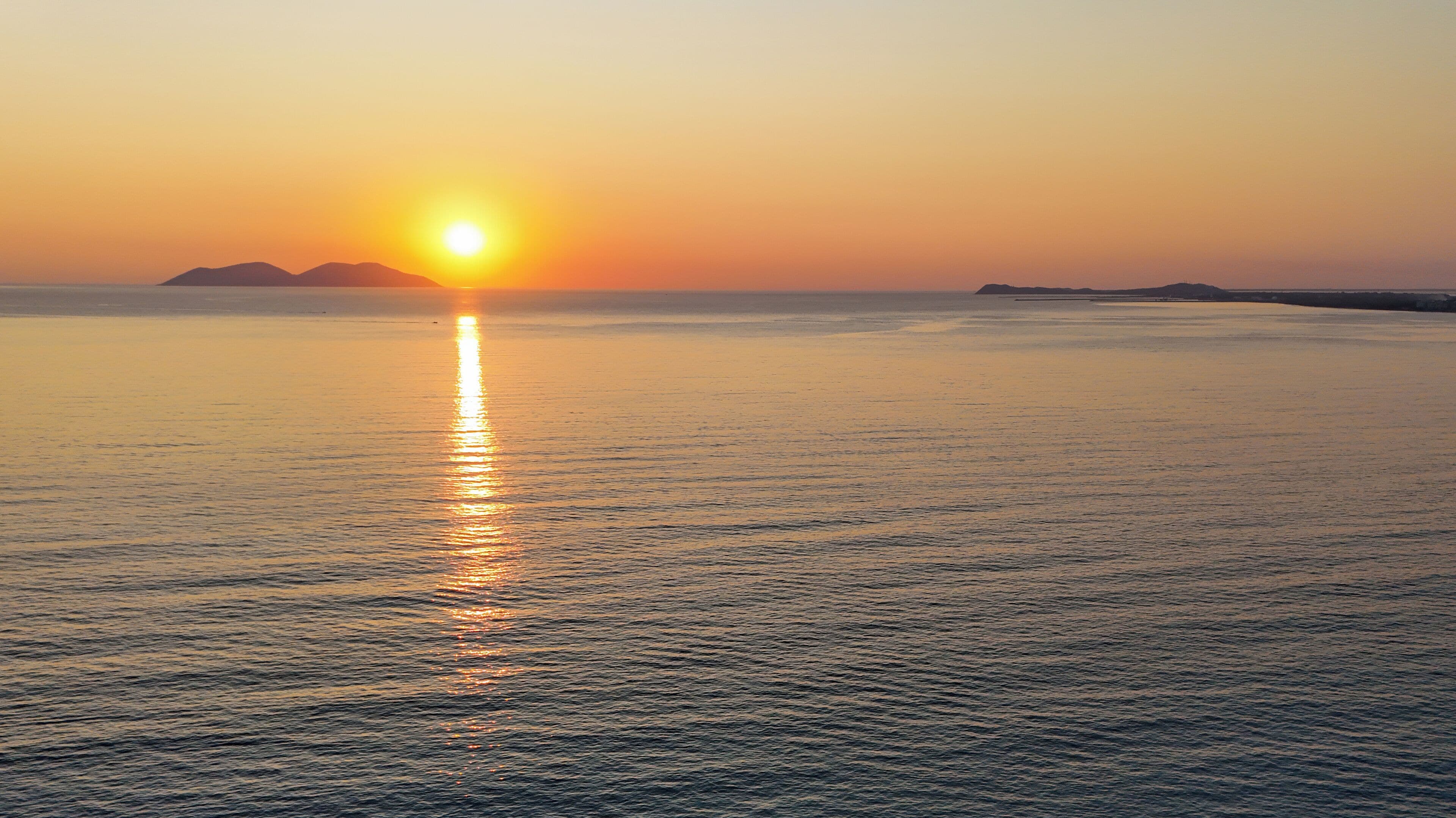 Un atardecer sobre un mar tranquilo con formas de tierra en la distancia.