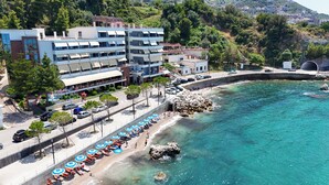 Ein Hotel an der Küste mit mehreren Etagen, ein Strand mit Sonnenschirmen und einer felsigen Uferlinie.