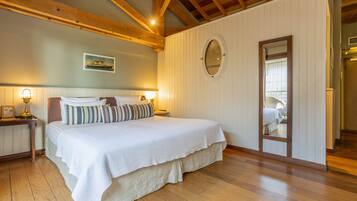 Une chambre avec un grand lit, des poutres en bois au plafond, une table de chevet avec une lampe et un miroir au mur.