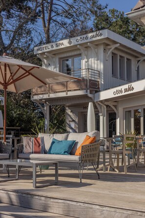 A hotel exterior with a lounge area featuring a sofa and chairs, an umbrella, and a sign reading "HOTEL & SPA."