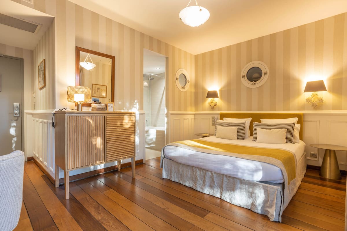 Una habitación de hotel con cama, mesitas de noche, un espejo y una ventana.