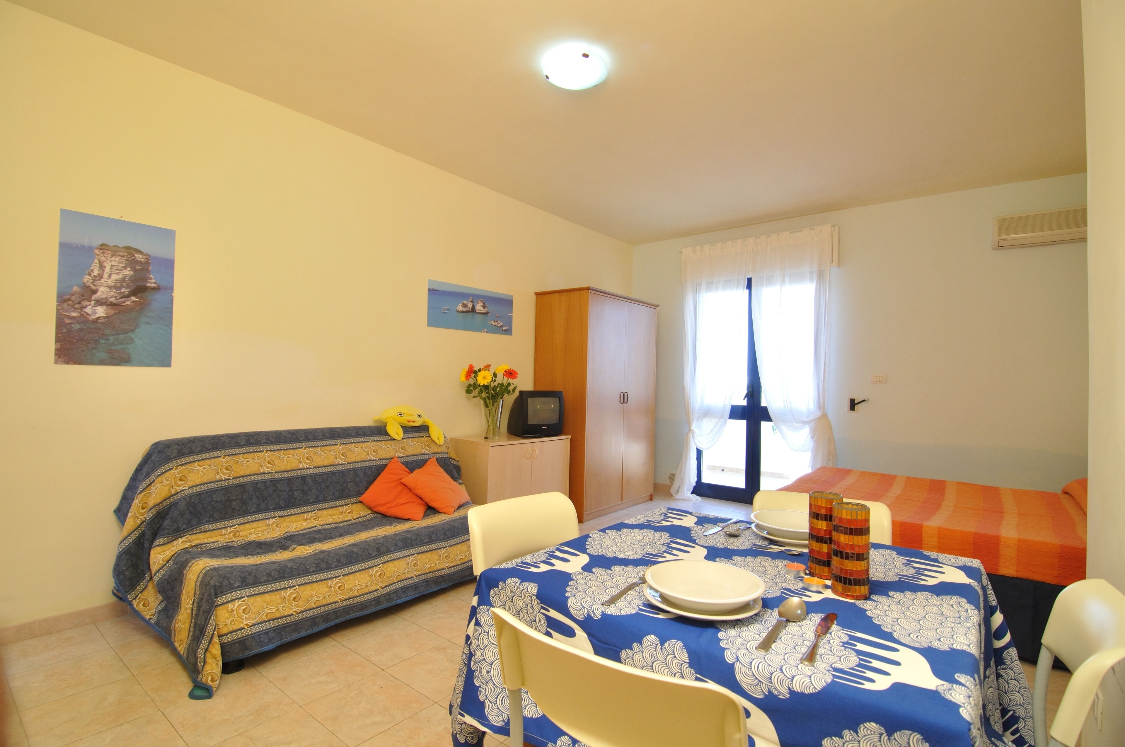 Habitació petita i ben il·luminada amb sofà, taula de dinar amb cadires, armari i finestra amb cortines.