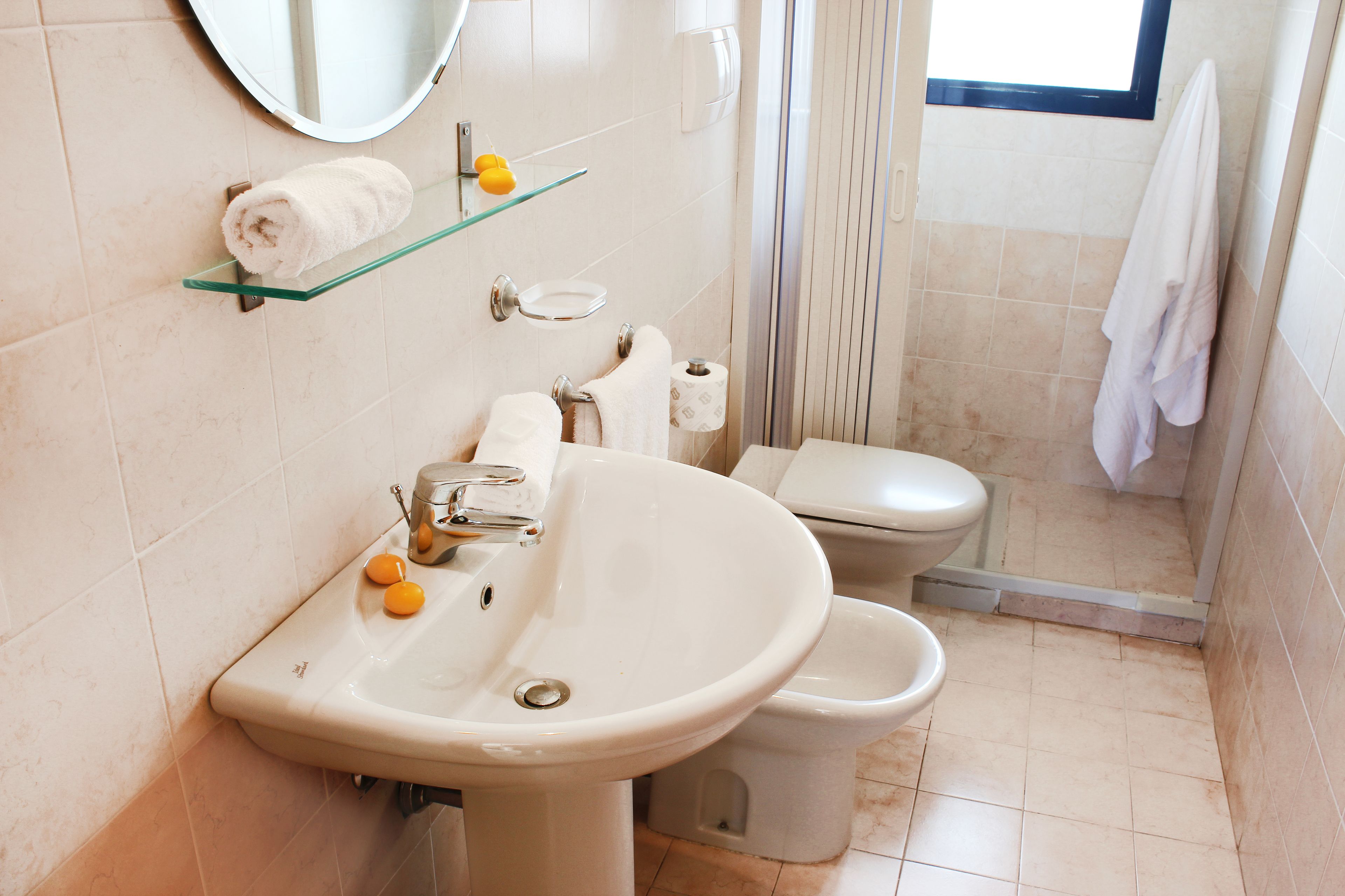 A bathroom with a sink, toilet, and a glass shelf with a towel and a yellow soap dispenser.