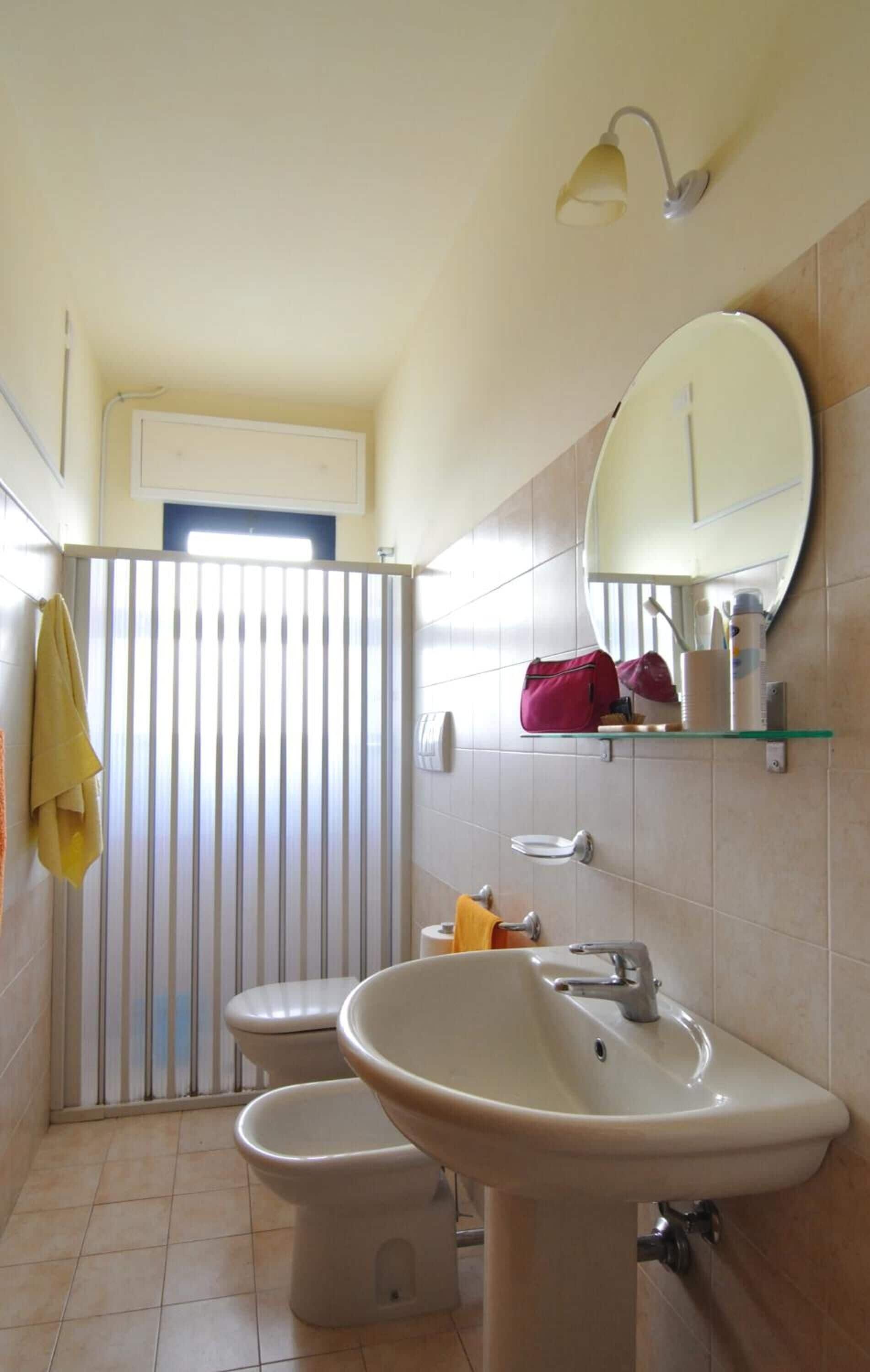 A bathroom with a toilet, bidet, sink, mirror, and towel rack.