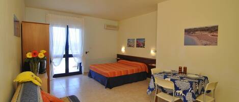 A bedroom with two beds, a dining table, and a sofa.
