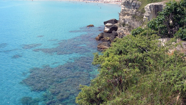 Blick auf die Küste mit klarem türkisblauem Wasser, steilen Felsen und einem historischen Stein-Turm.