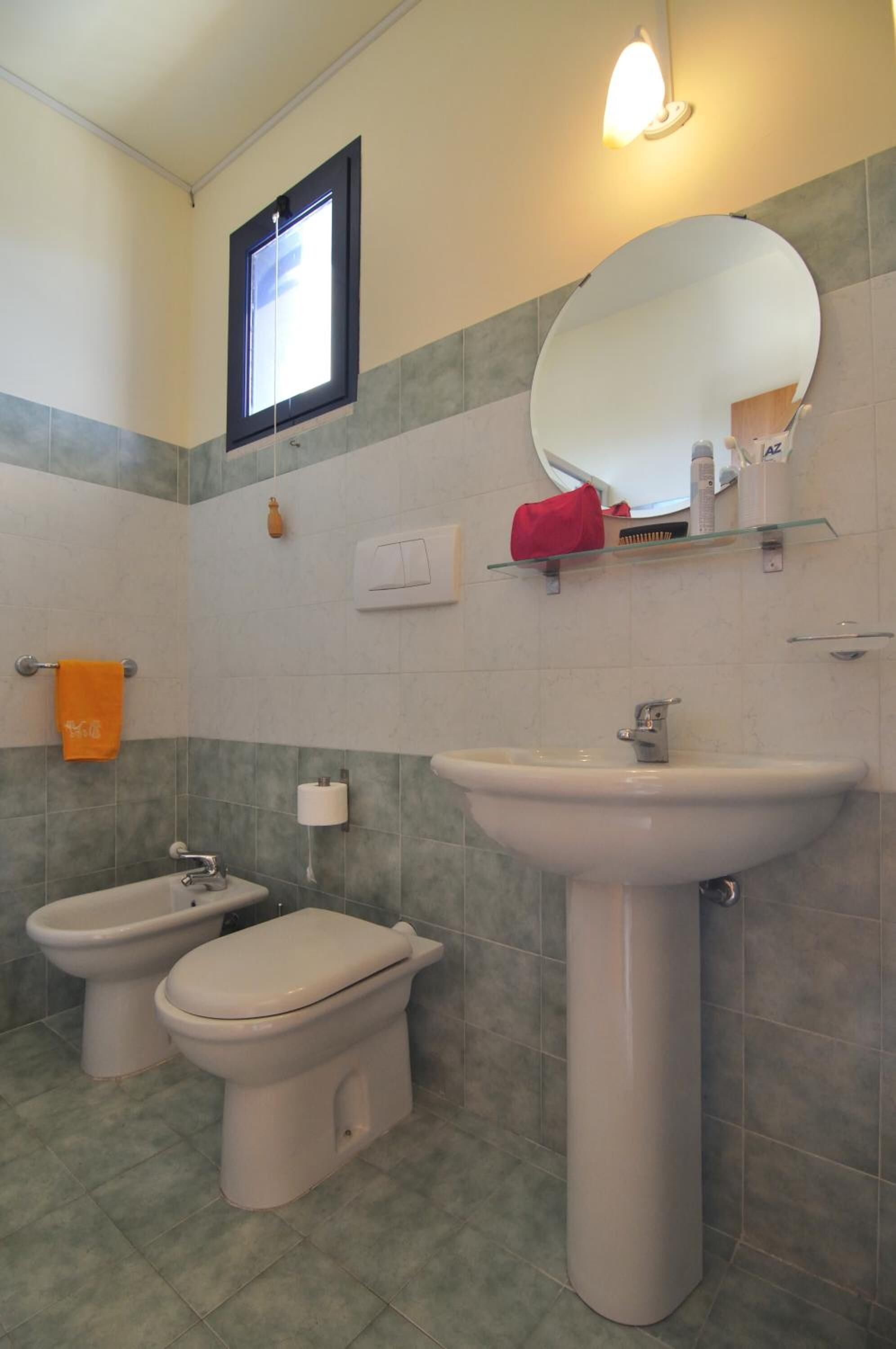 A bathroom with two toilets, a sink, a mirror, and a window.