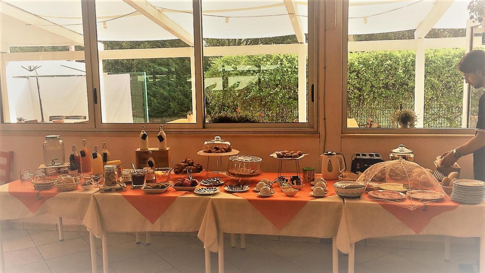 Een buffet met diverse gerechten en drankjes, opgesteld in een tentachtige ruimte met grote ramen.