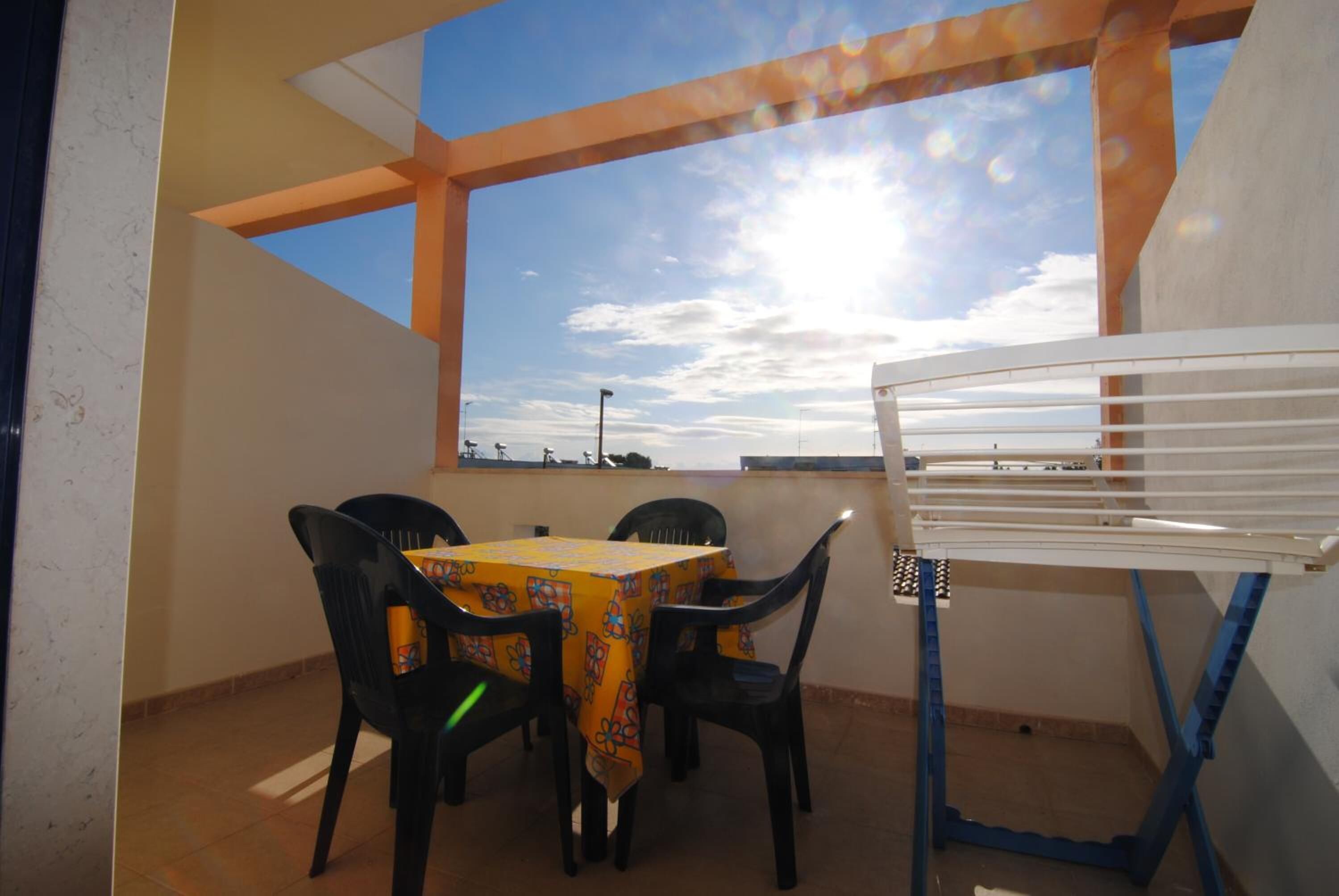 A balcony with a table and chairs, a drying rack, and a view of the sky.