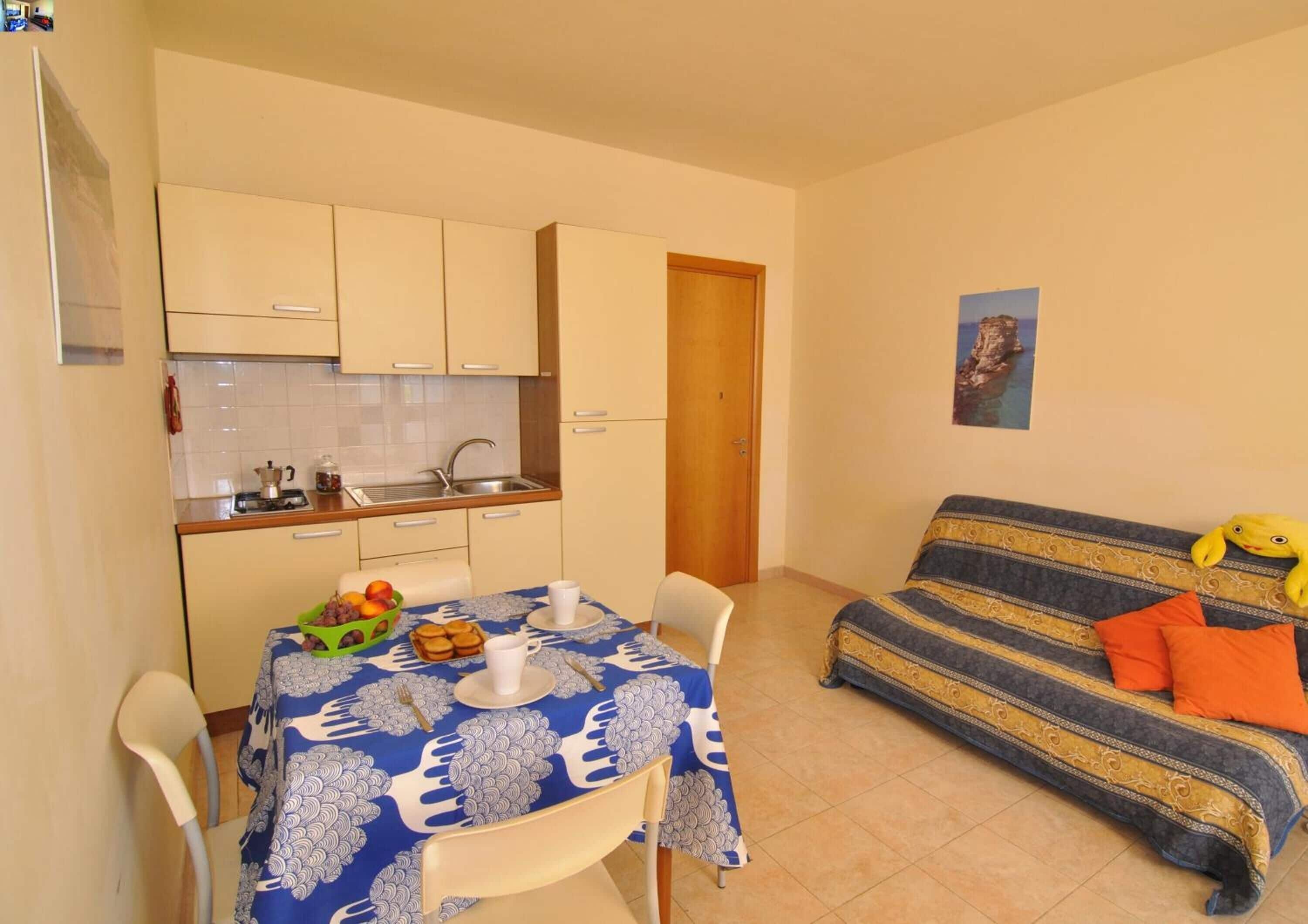 A compact living space with a kitchenette, a dining table with a blue tablecloth, and a sofa with patterned cushions.