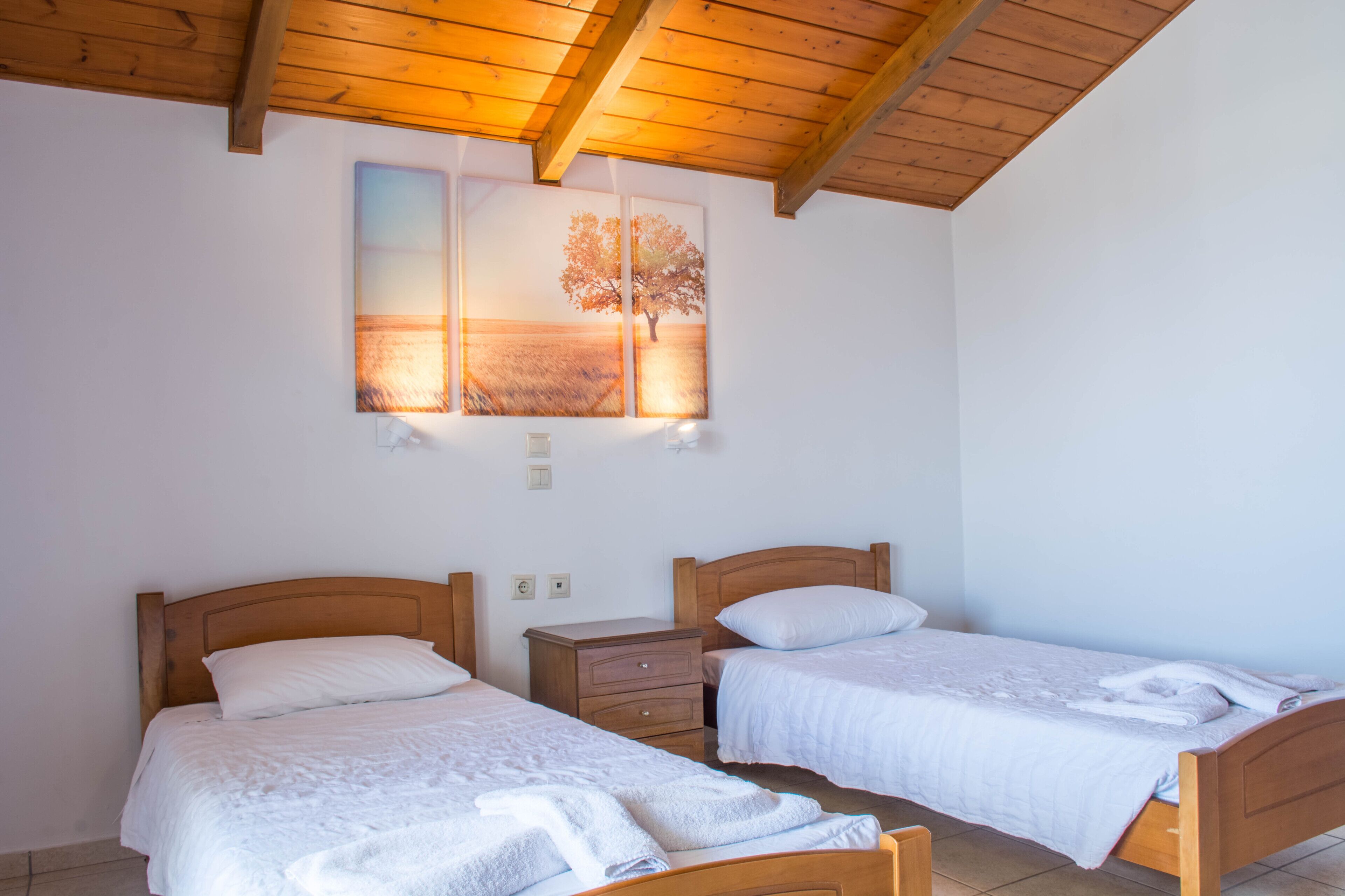 A room with two wooden beds, a nightstand, and a wall-mounted artwork depicting a tree and landscape.