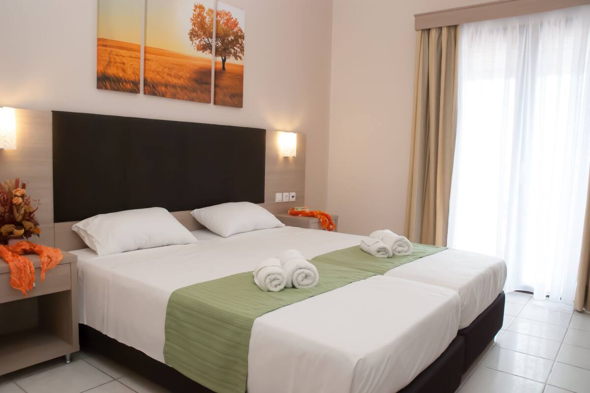 A hotel room with a large bed, two bedside tables, a headboard, and a window with curtains.