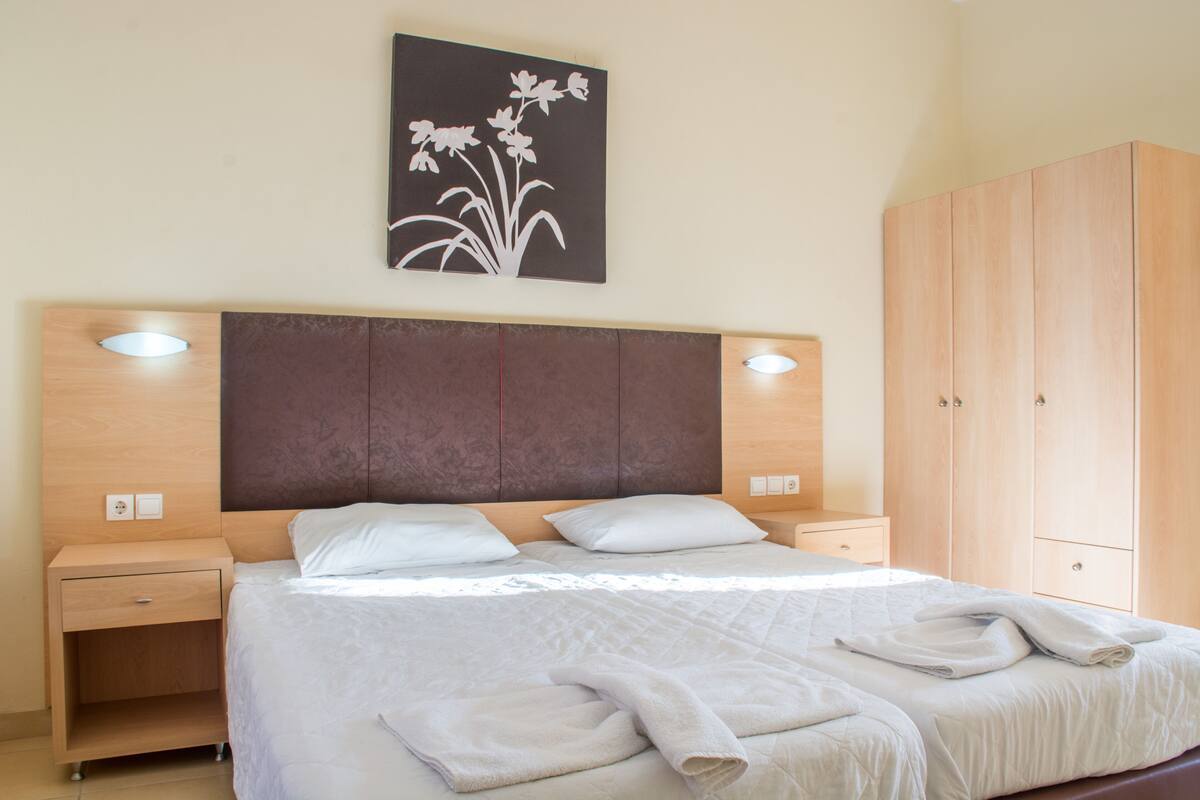 A bedroom with a large bed, wooden headboard, bedside tables, a wardrobe, and a wall-mounted light fixture.