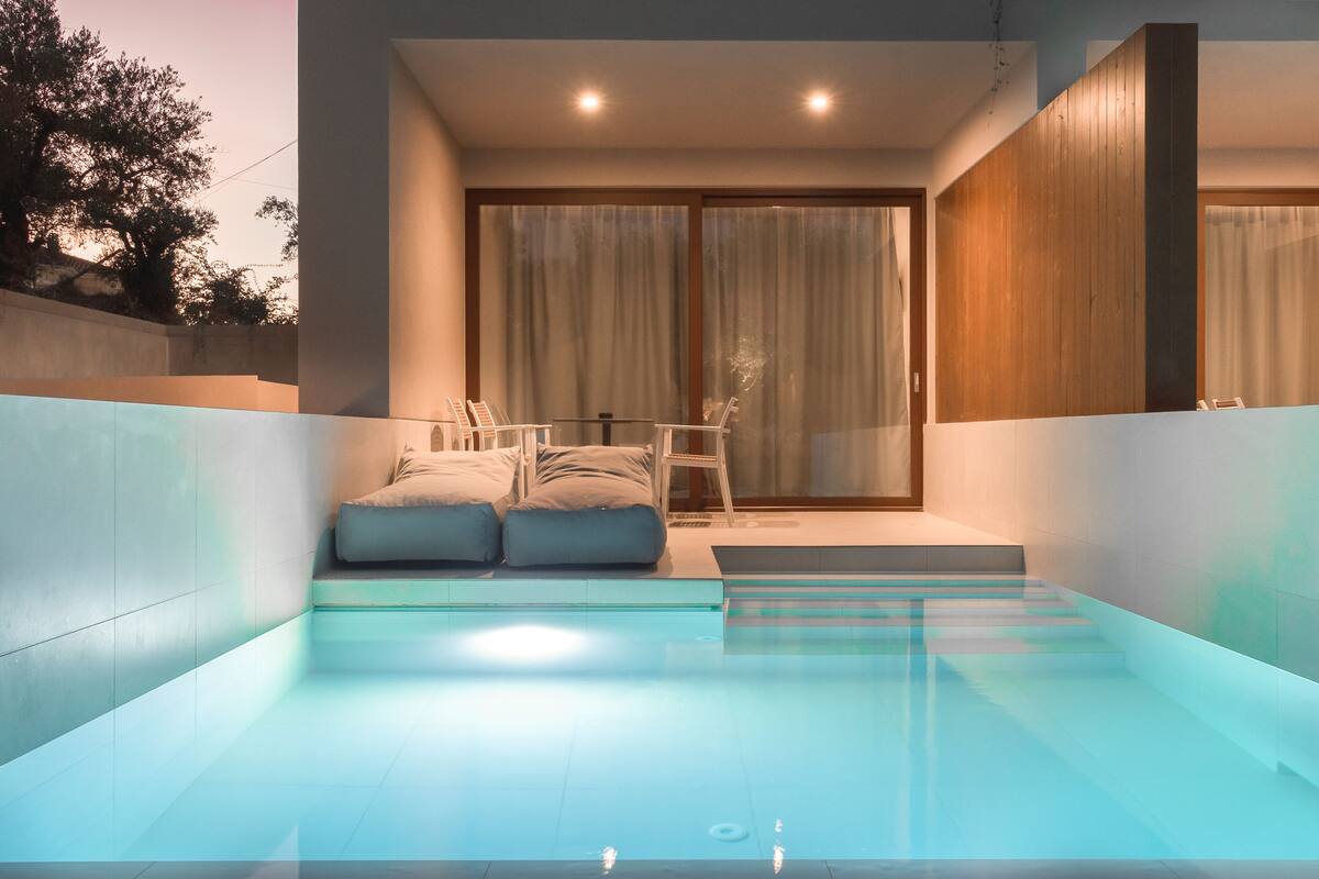 A modern indoor pool with a glass barrier, a seating area with cushions, and a wooden wall.