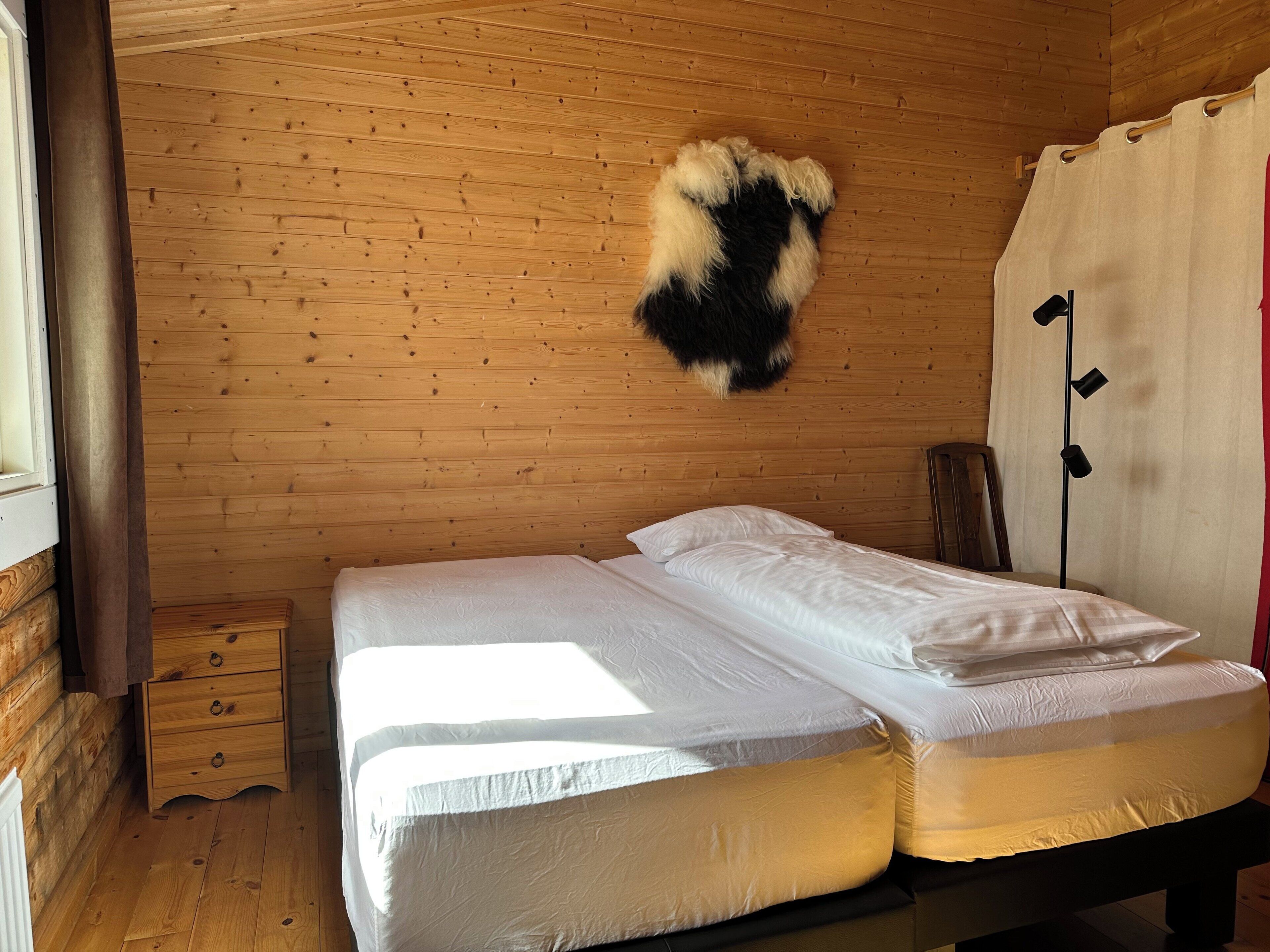 Une pièce de style cabane en bois, avec un lit, une petite commode en bois et un tapis en fourrure accroché au mur.