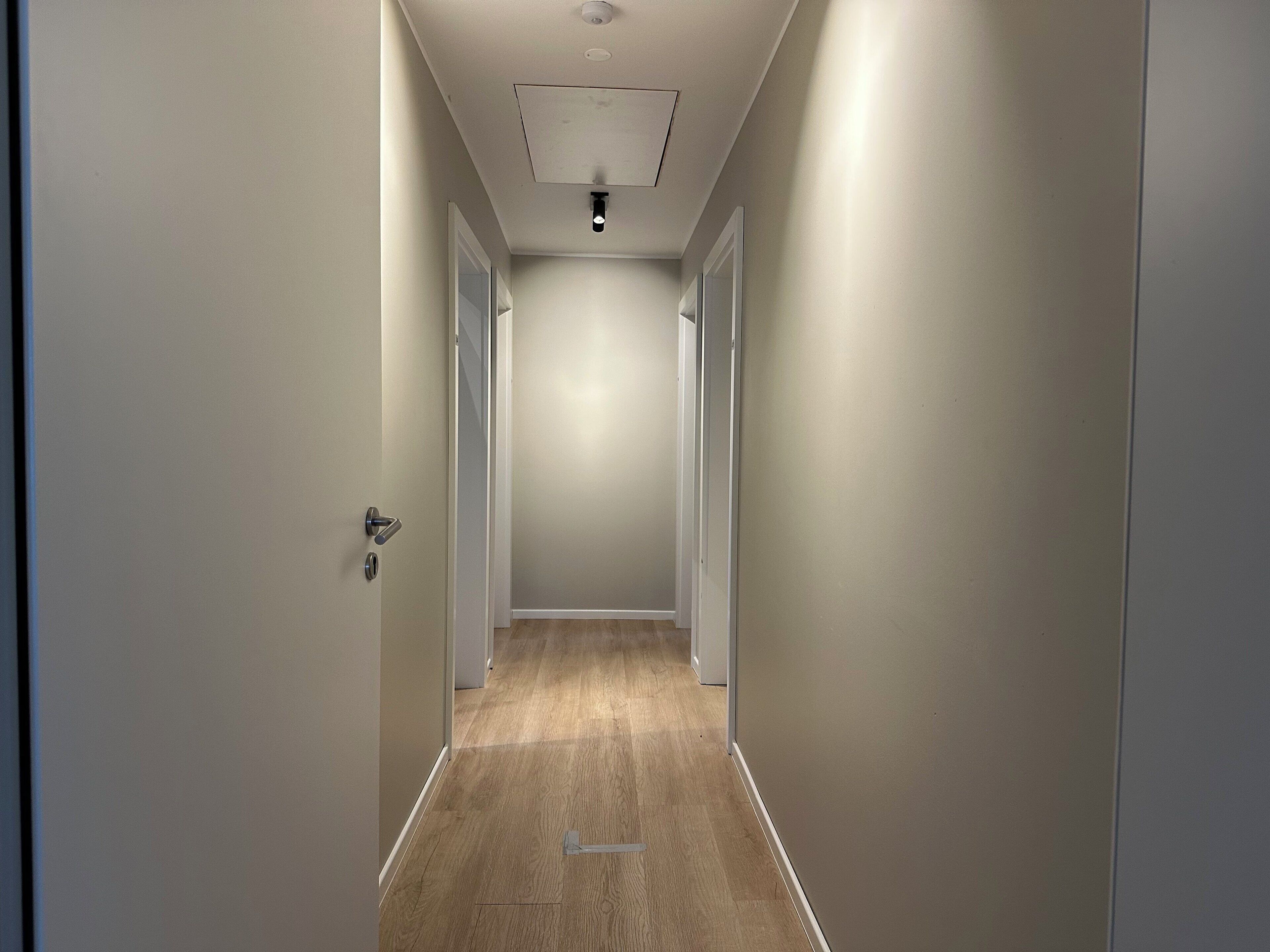 A hallway with a light-colored floor and walls, leading to a door at the end.