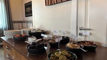 Una mesa de buffet con diversos alimentos y condimentos, incluyendo ensaladas, pepinillos y un recipiente con col roja.