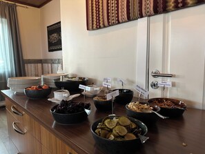 A buffet table with various food items and condiments, including bowls of salad, pickles, and a dish labeled 'Red Cabbage.'