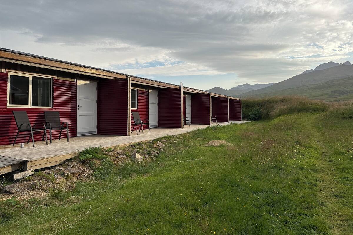 Eine Reihe roter Hütten mit einer Holzdiele und Stühlen vor einer Kulisse aus grünen Hügeln und Bergen.