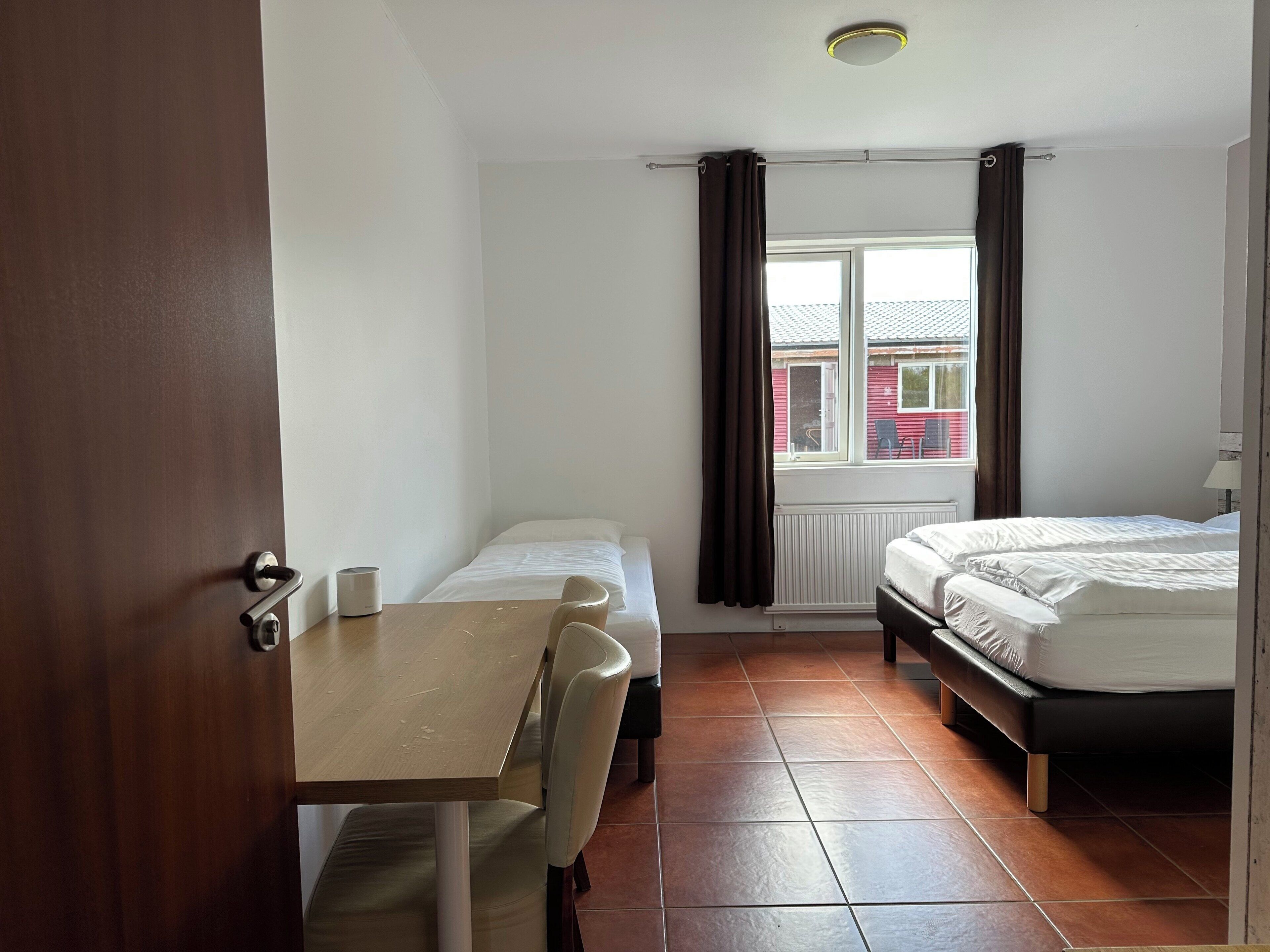 Habitación de hotel con cama, una mesita, una silla y ventana con cortinas.