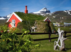 A red house with a white roof, a small shed, and a wooden fence in a grassy field with a mountain in the background. - Alfheimar Hotel (Borgarfjordur Eystri)