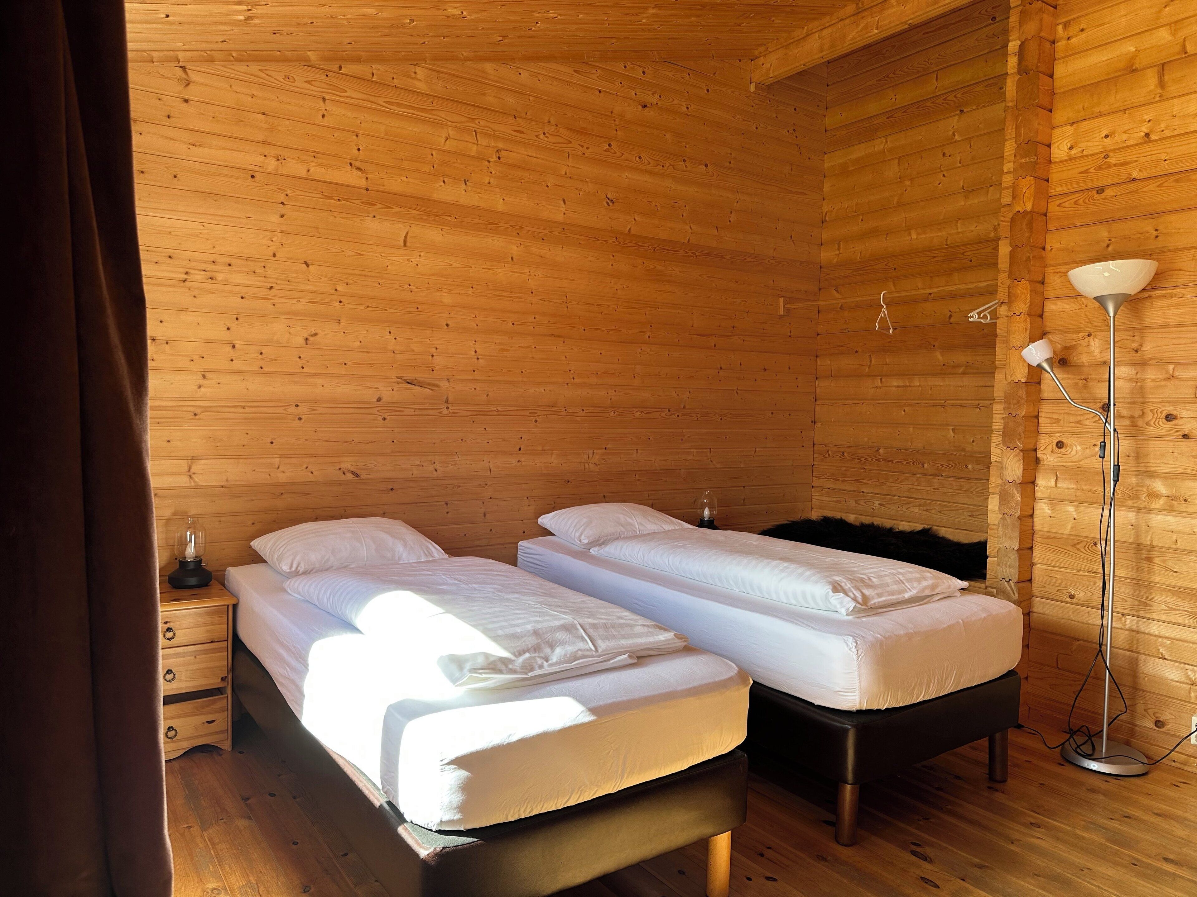 Een houten kamer met twee bedden, een nachtkastje, een lamp en een ladekast.