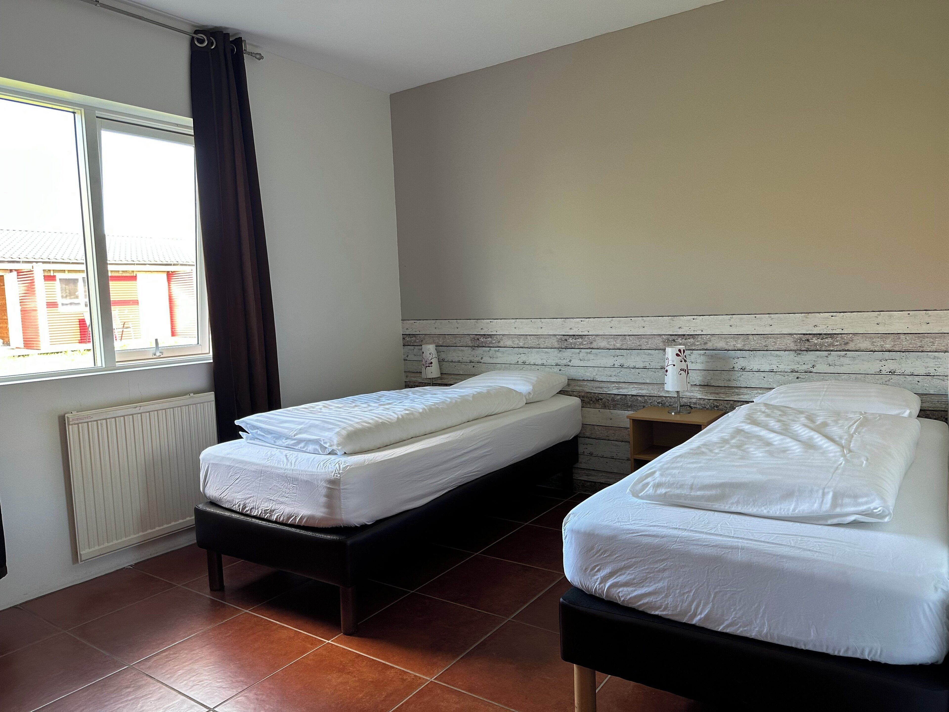 A room with two beds, a window with curtains, a radiator, and a wooden headboard.