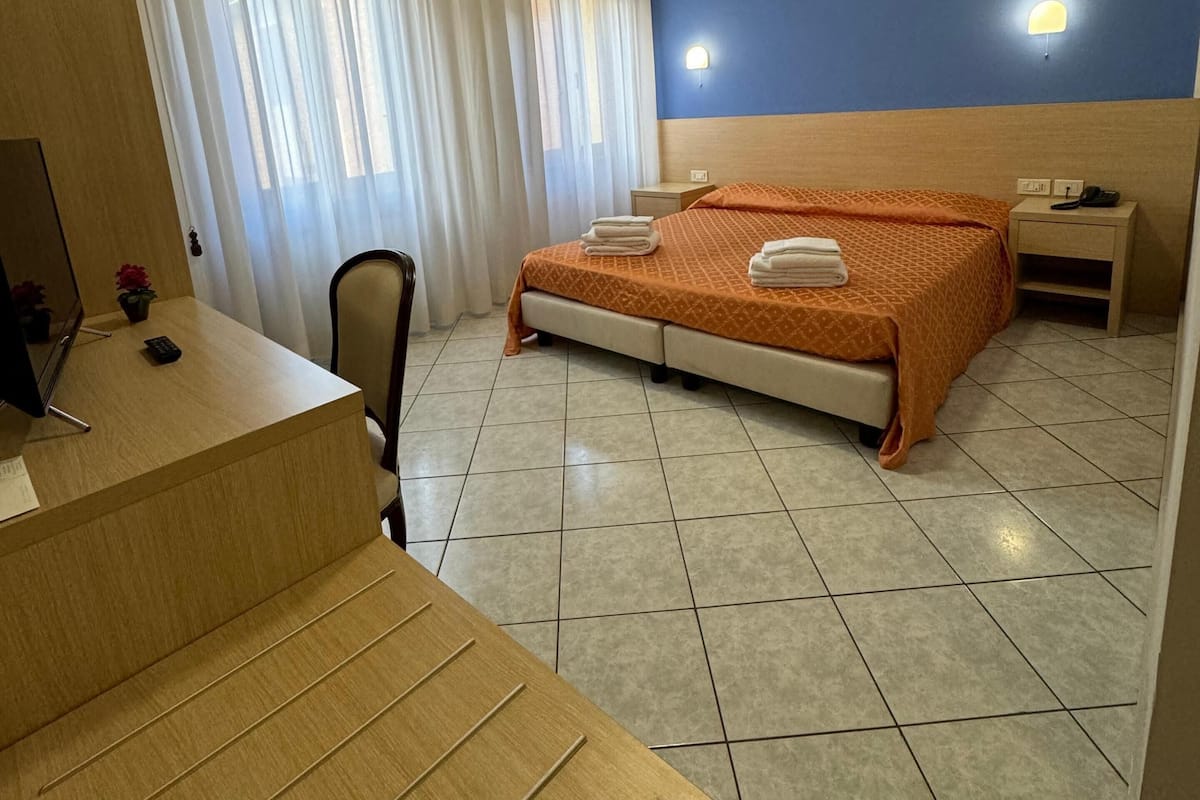 A hotel room with a bed, a desk, a chair, a nightstand, and a telephone.