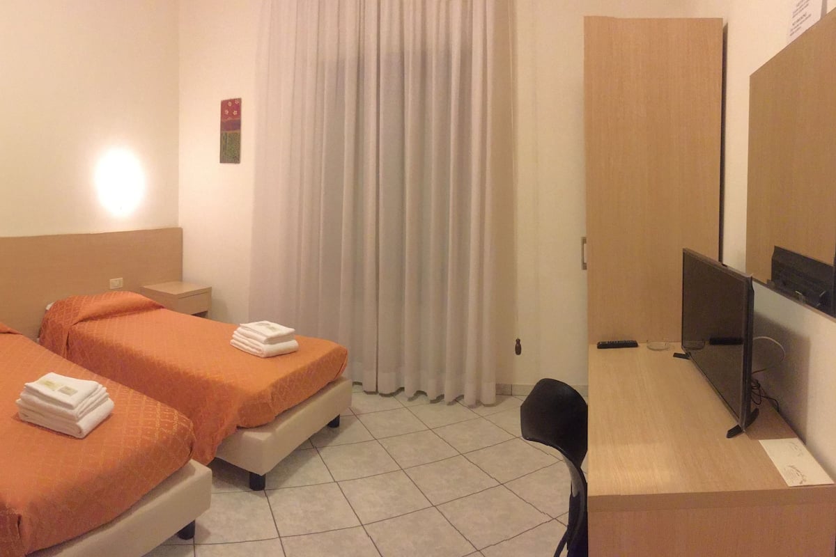 A hotel room with two beds, a desk, a chair, and a TV.