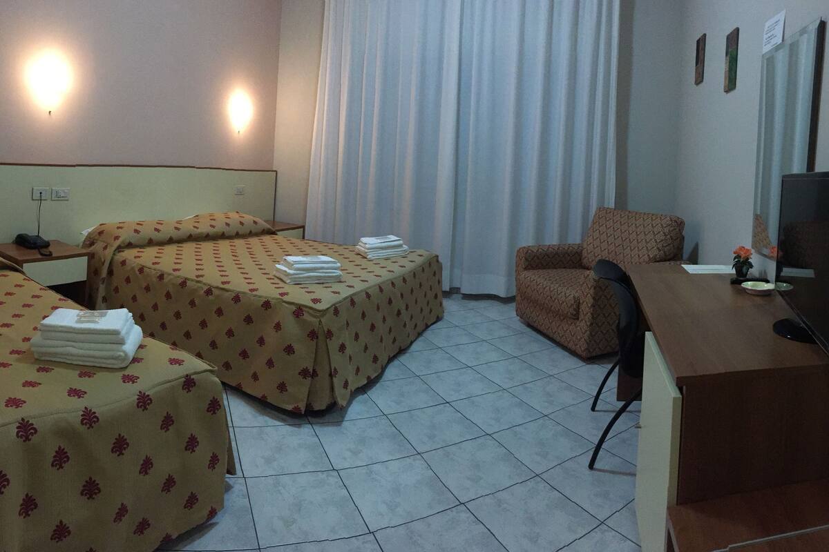 A hotel room with two beds, a desk, a chair, a TV, and a window with curtains.