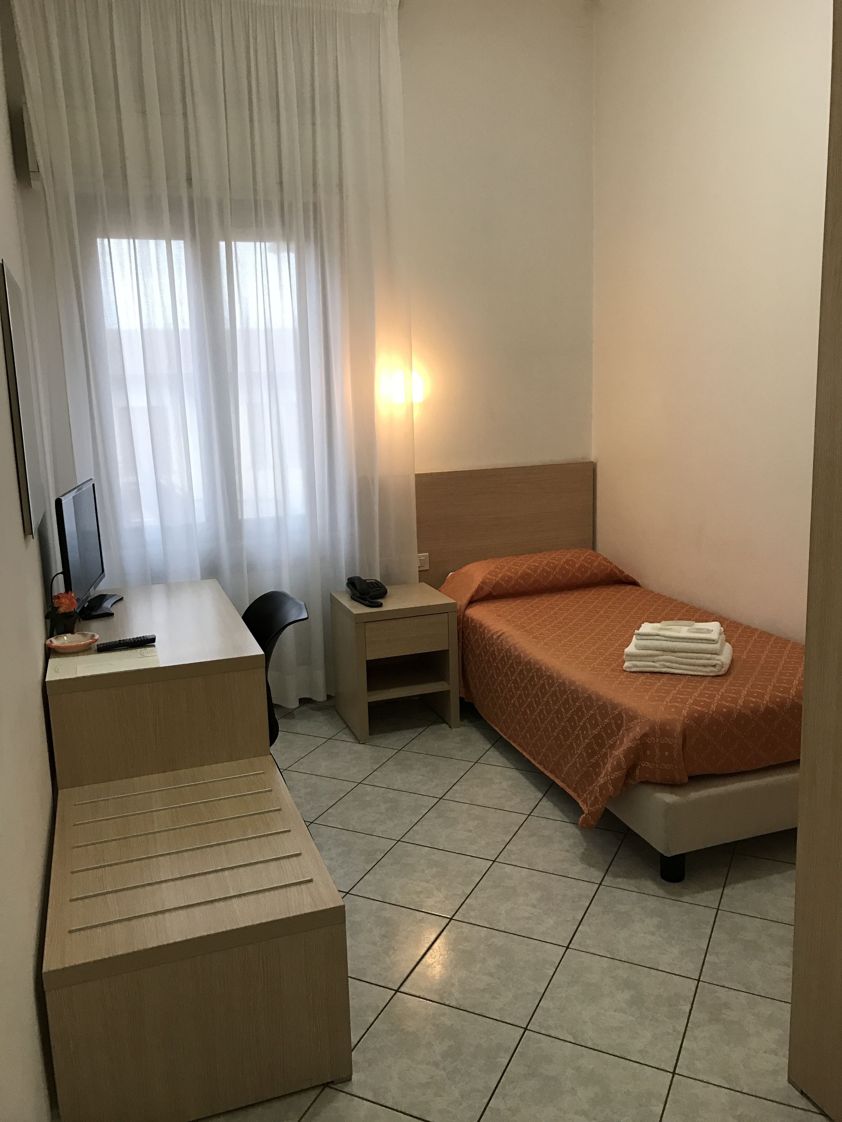 Una habitación de hotel pequeña con una cama, un escritorio, una silla, una mesita de noche y un televisor.