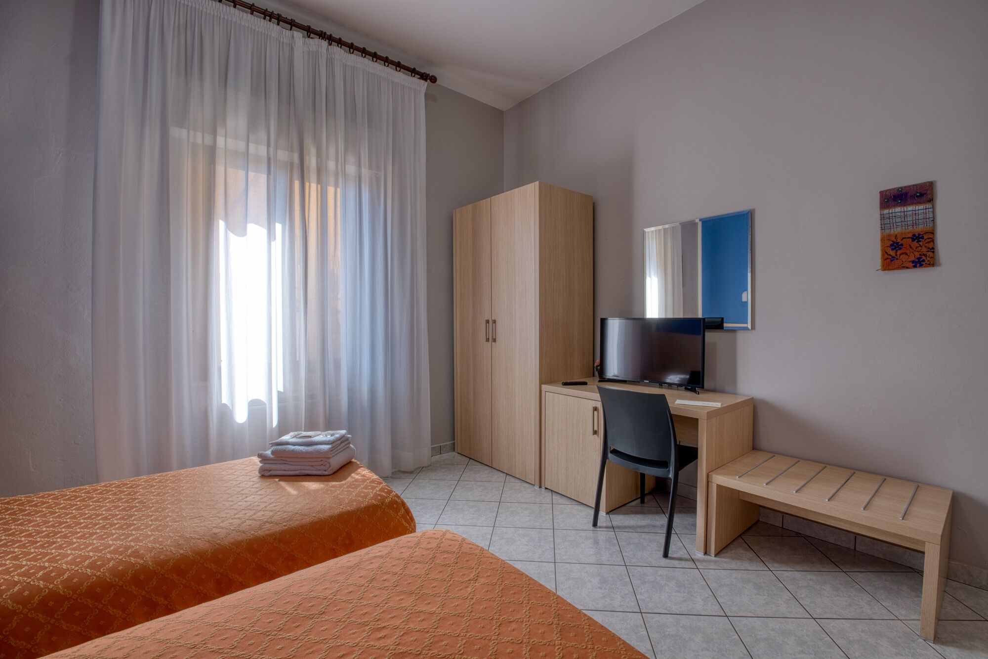 A hotel room with a bed, a desk with a chair, a wardrobe, and a television.