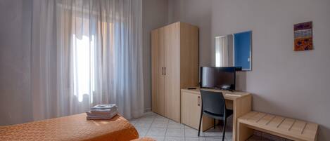 A hotel room with a bed, a desk with a chair, a wardrobe, and a television.