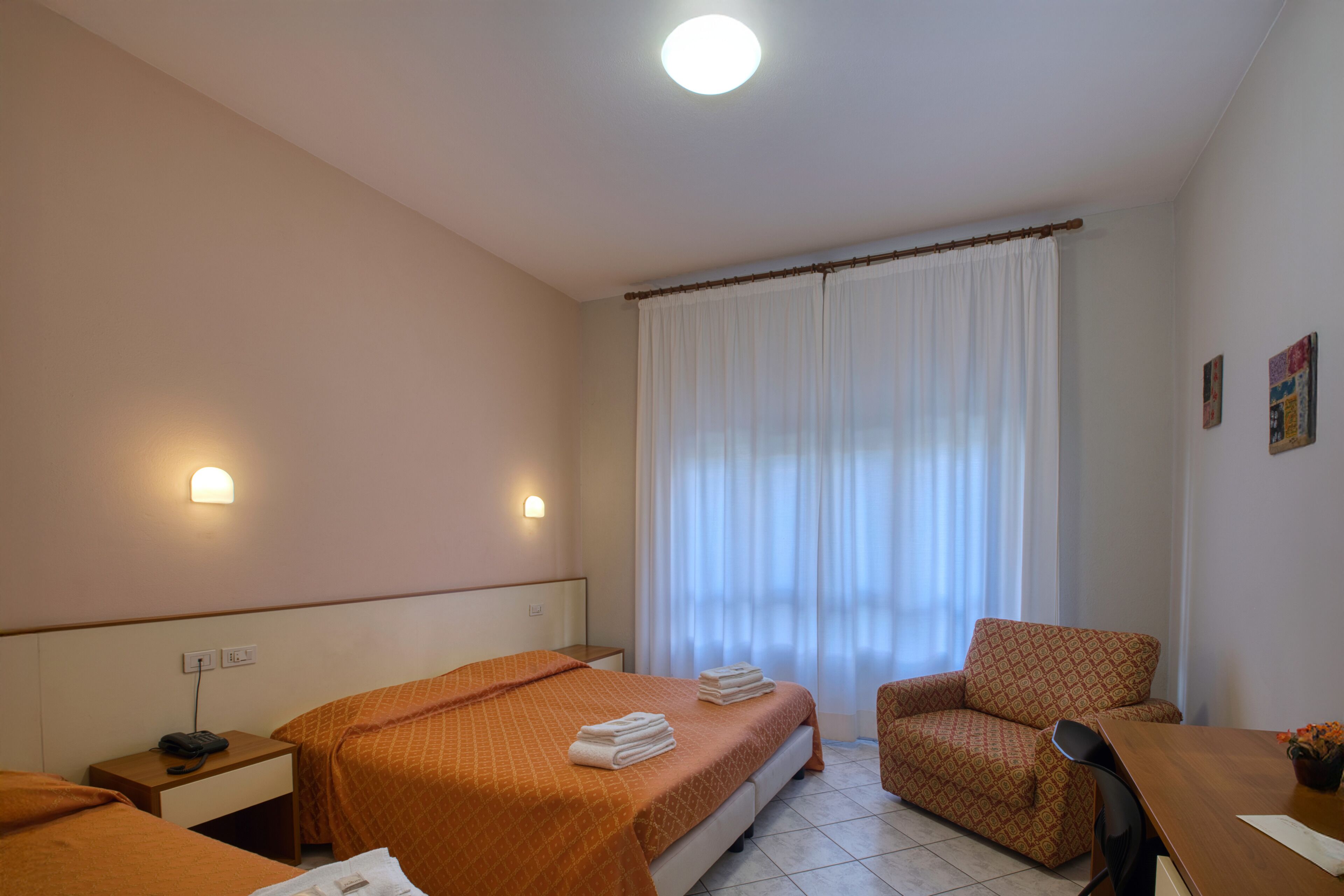 A hotel room with two beds, a chair, a desk, and a window with curtains.